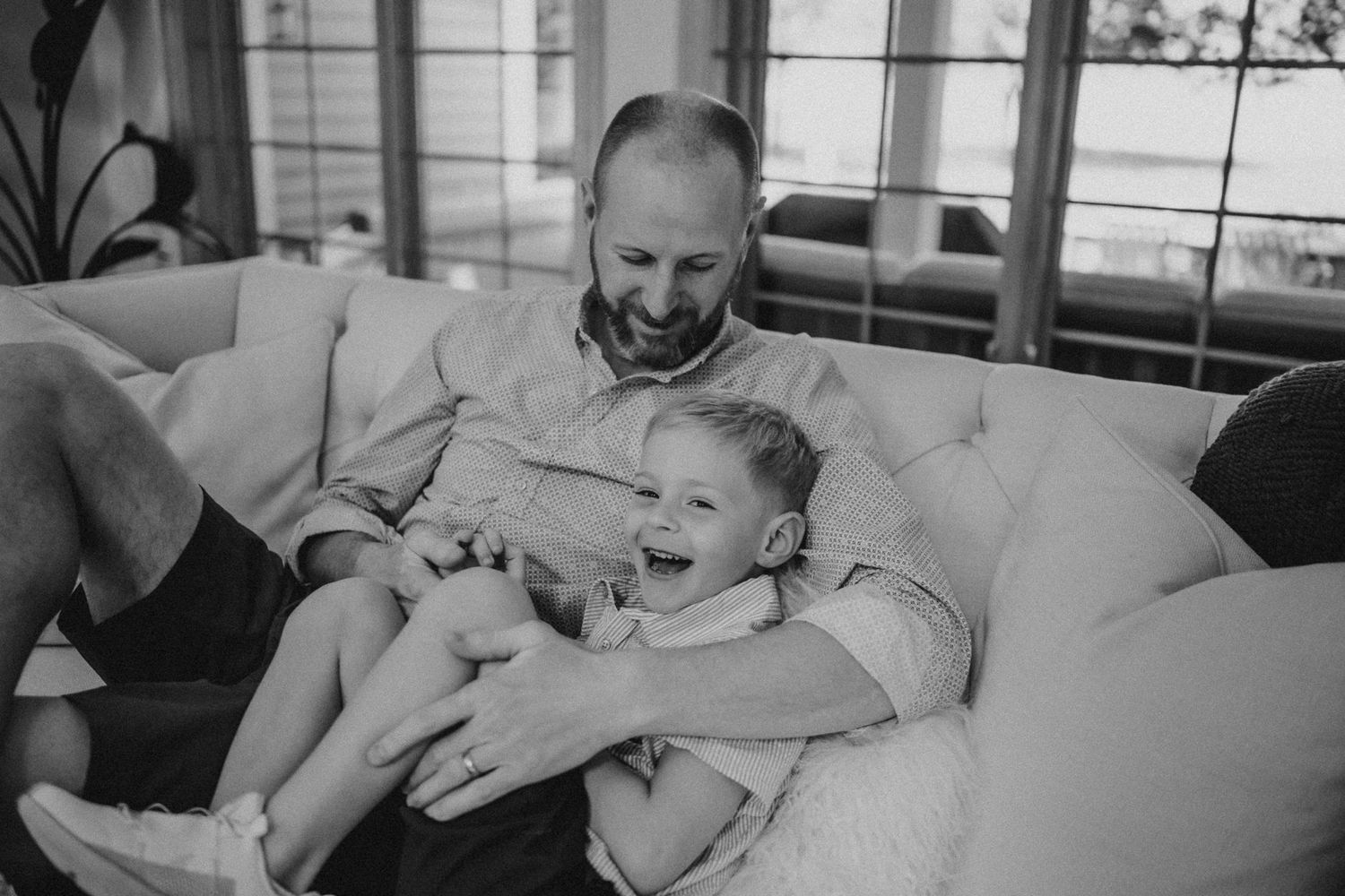 Black and white photo showing joyful bonding moment on a plush sofa.