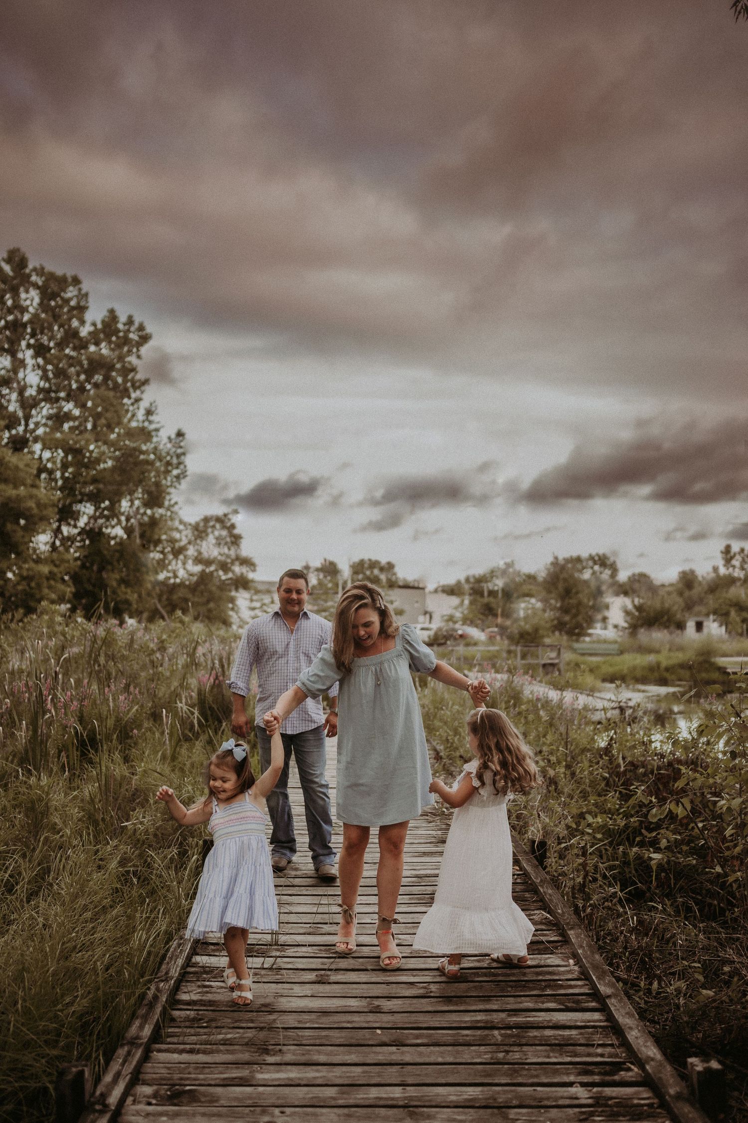Family walking together on a wooden pathway during golden hour with dramatic clouds overhead.