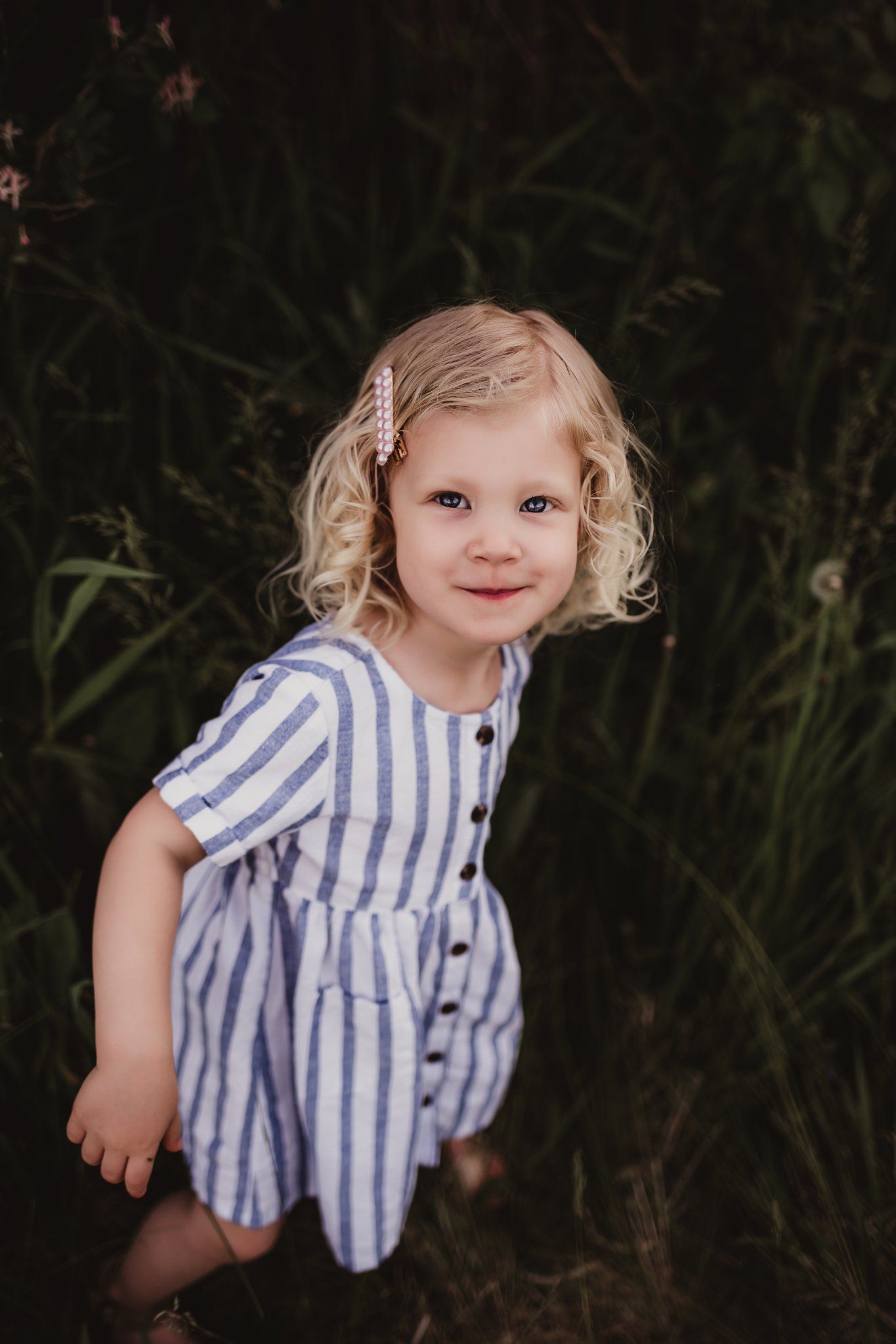 A young child in a blue and white striped dress poses outdoors against a dark background.