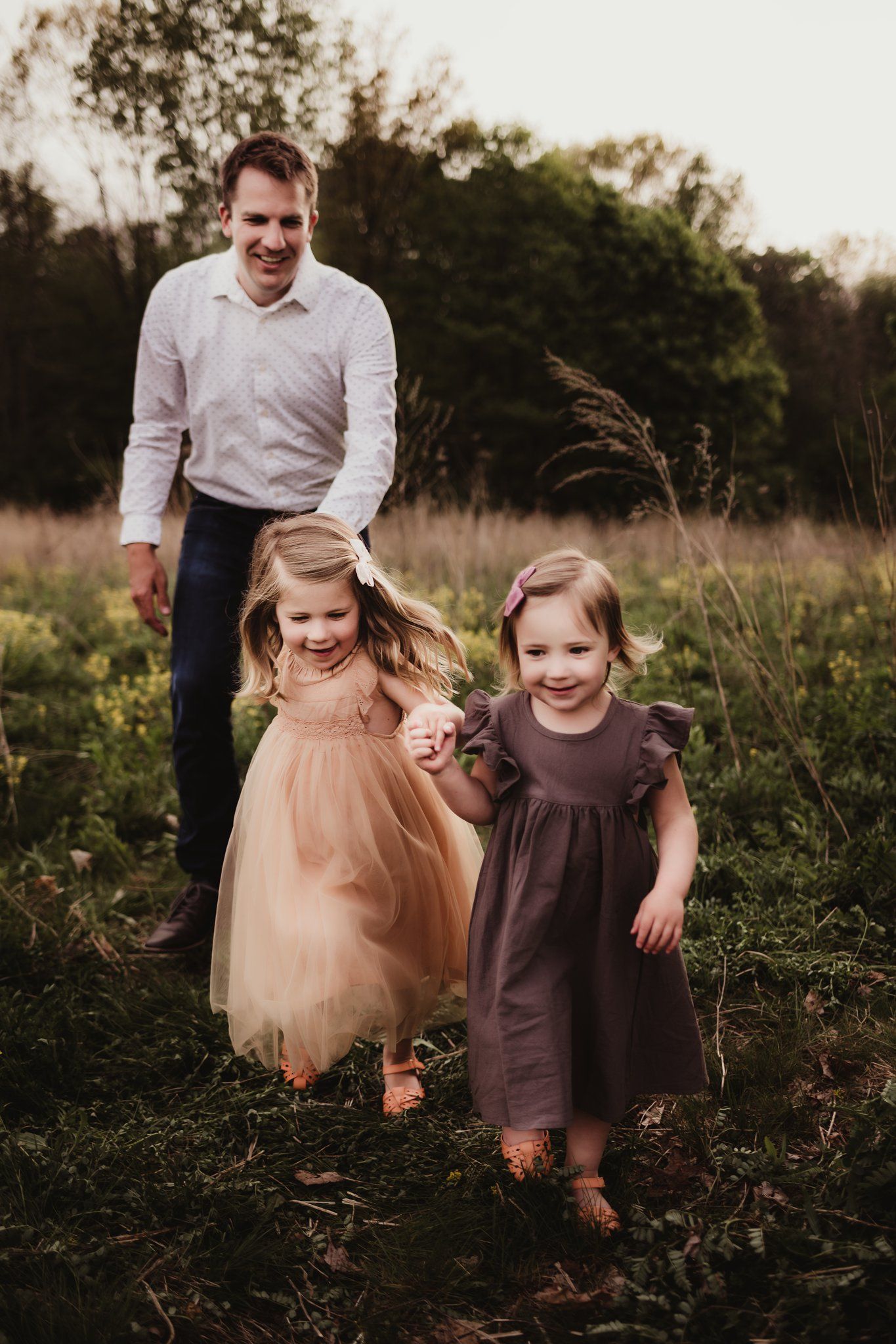 Family walking through tall grass at sunset in coordinated neutral tones.