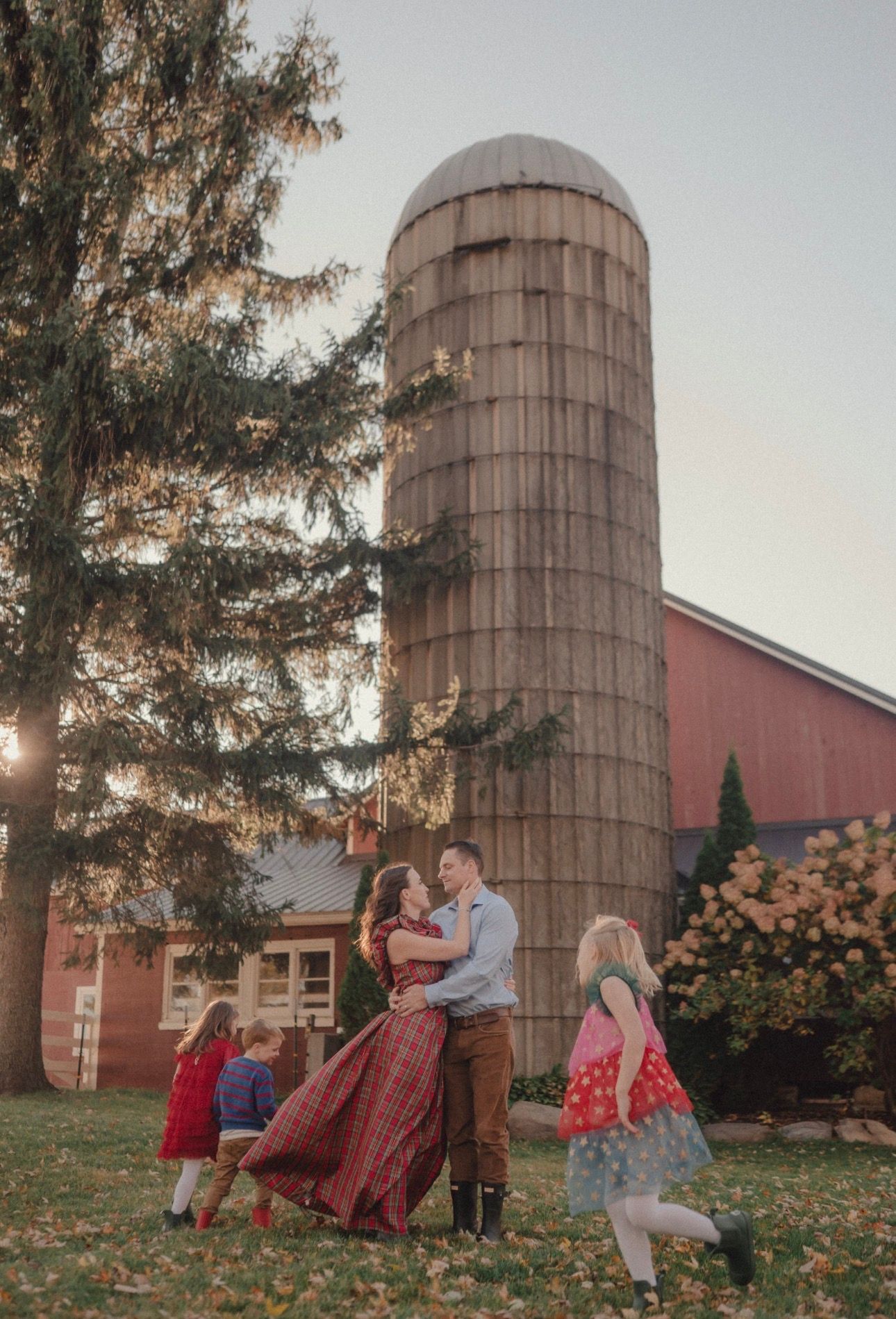 Playful photo session near rustic barn silos during sunset.