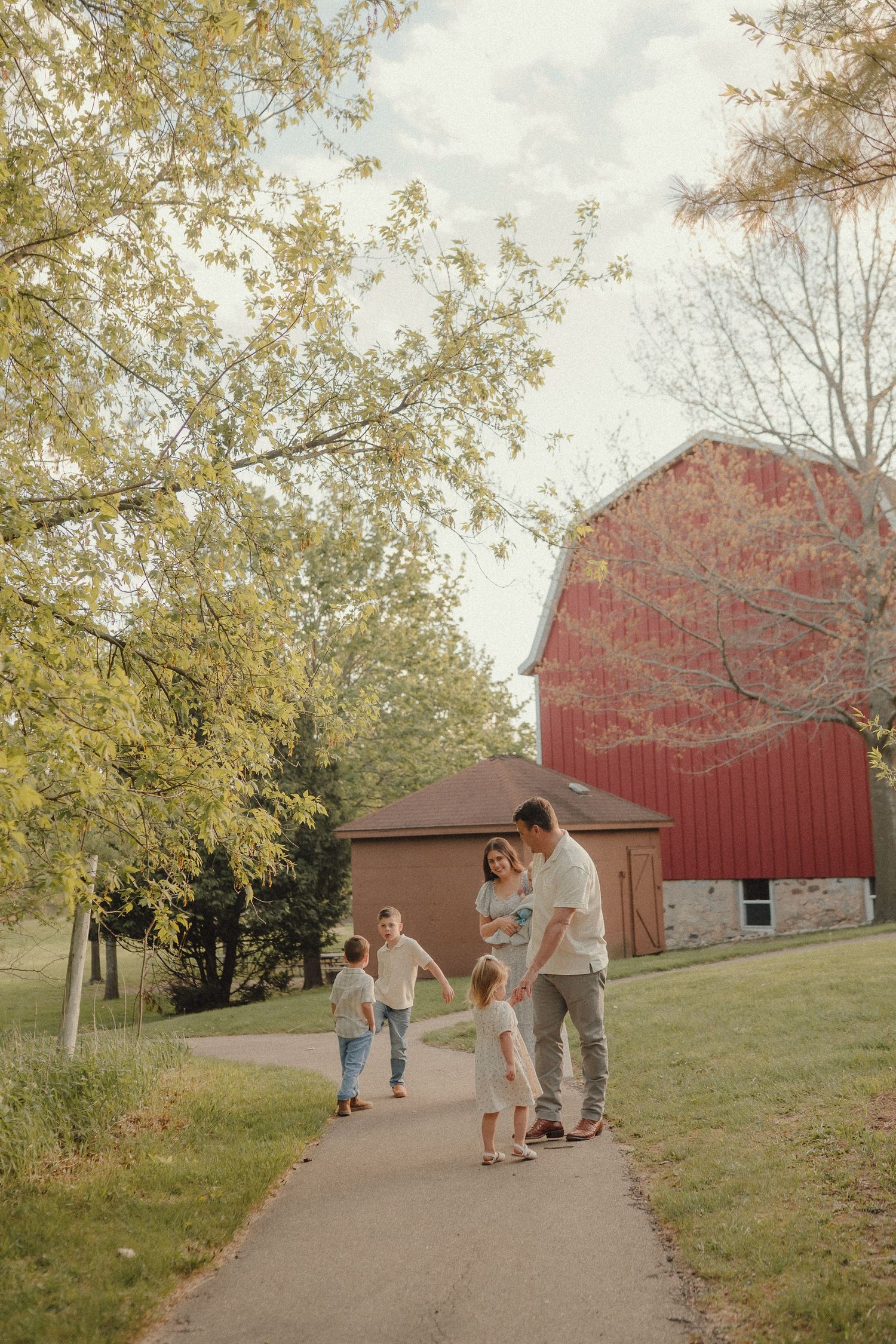 Family of five walking on a path near a red barn surrounded by autumn trees.