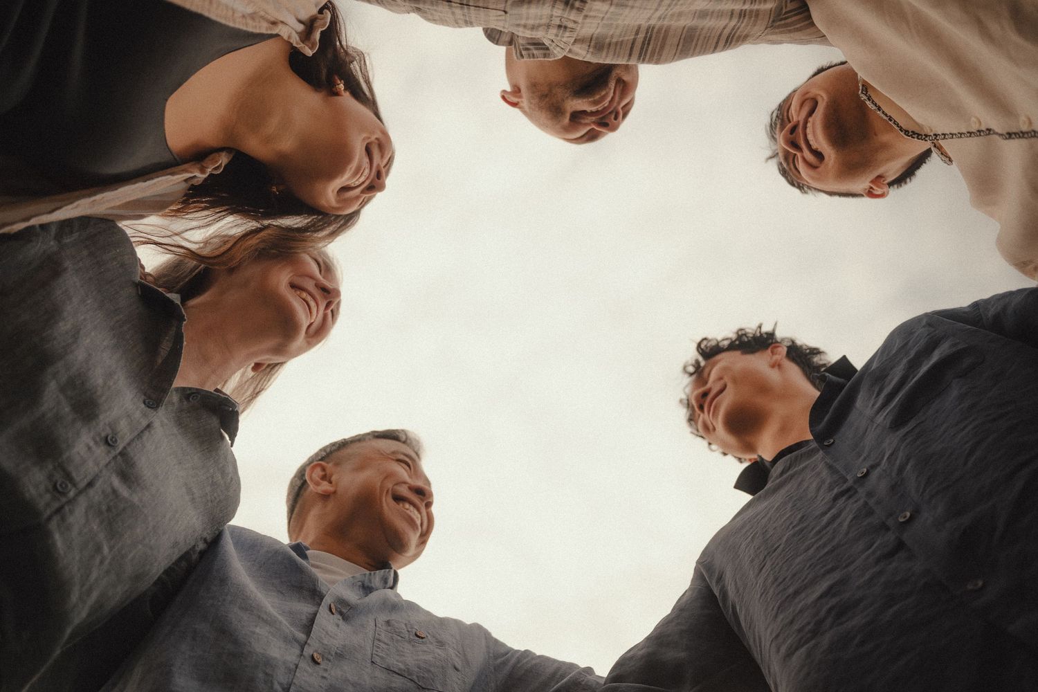 Group of people huddled together in a circle viewed from below, symbolizing teamwork and unity.