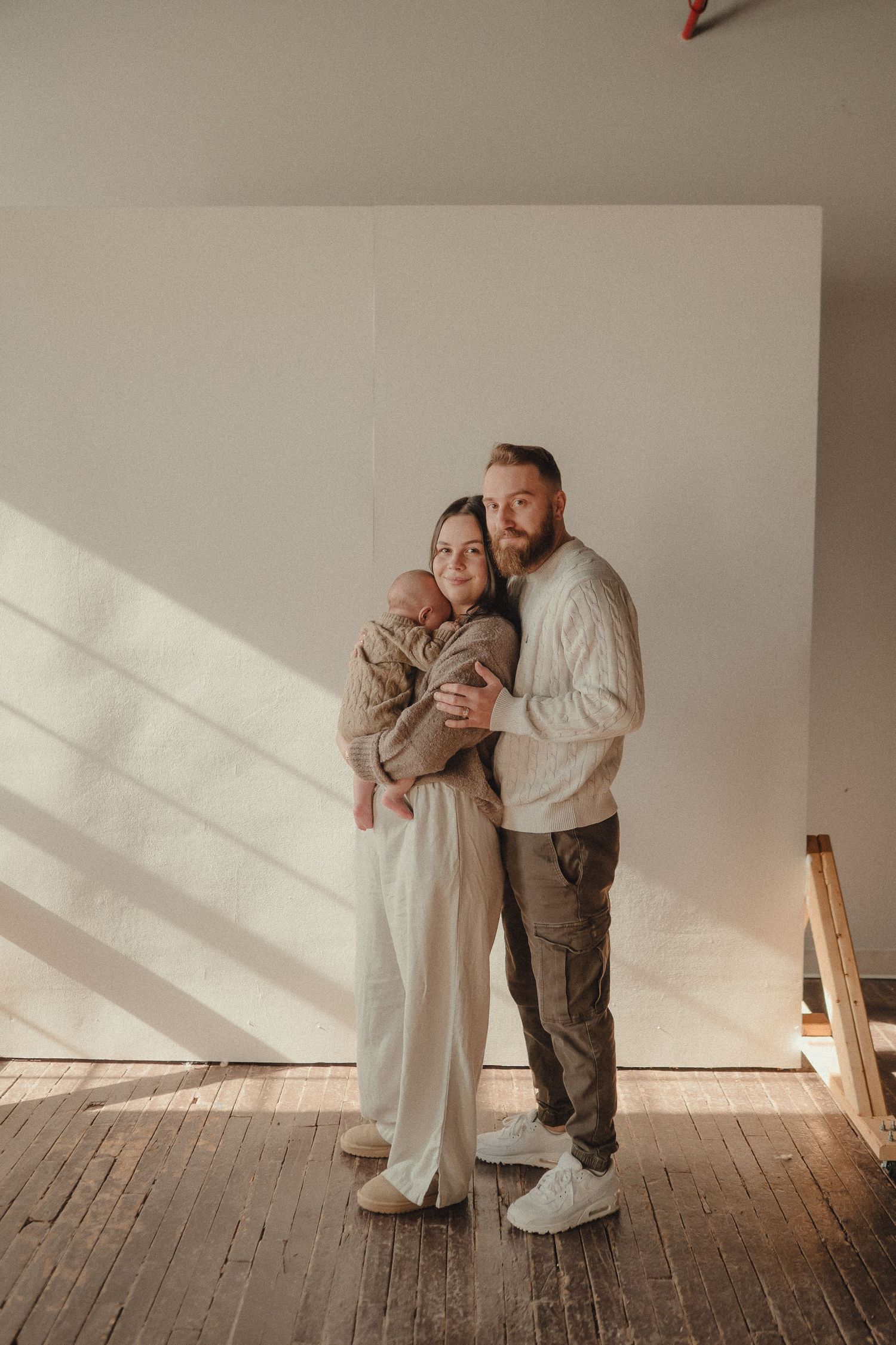 Minimalist family portrait session against white wall with dramatic window light.