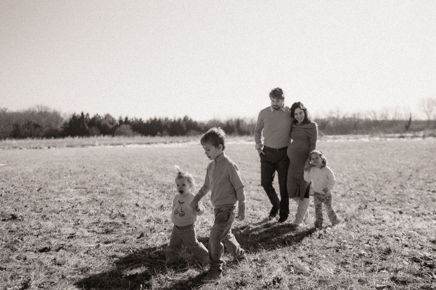 Black and white photo of a family and their dog walking together in an open field on a sunny day.