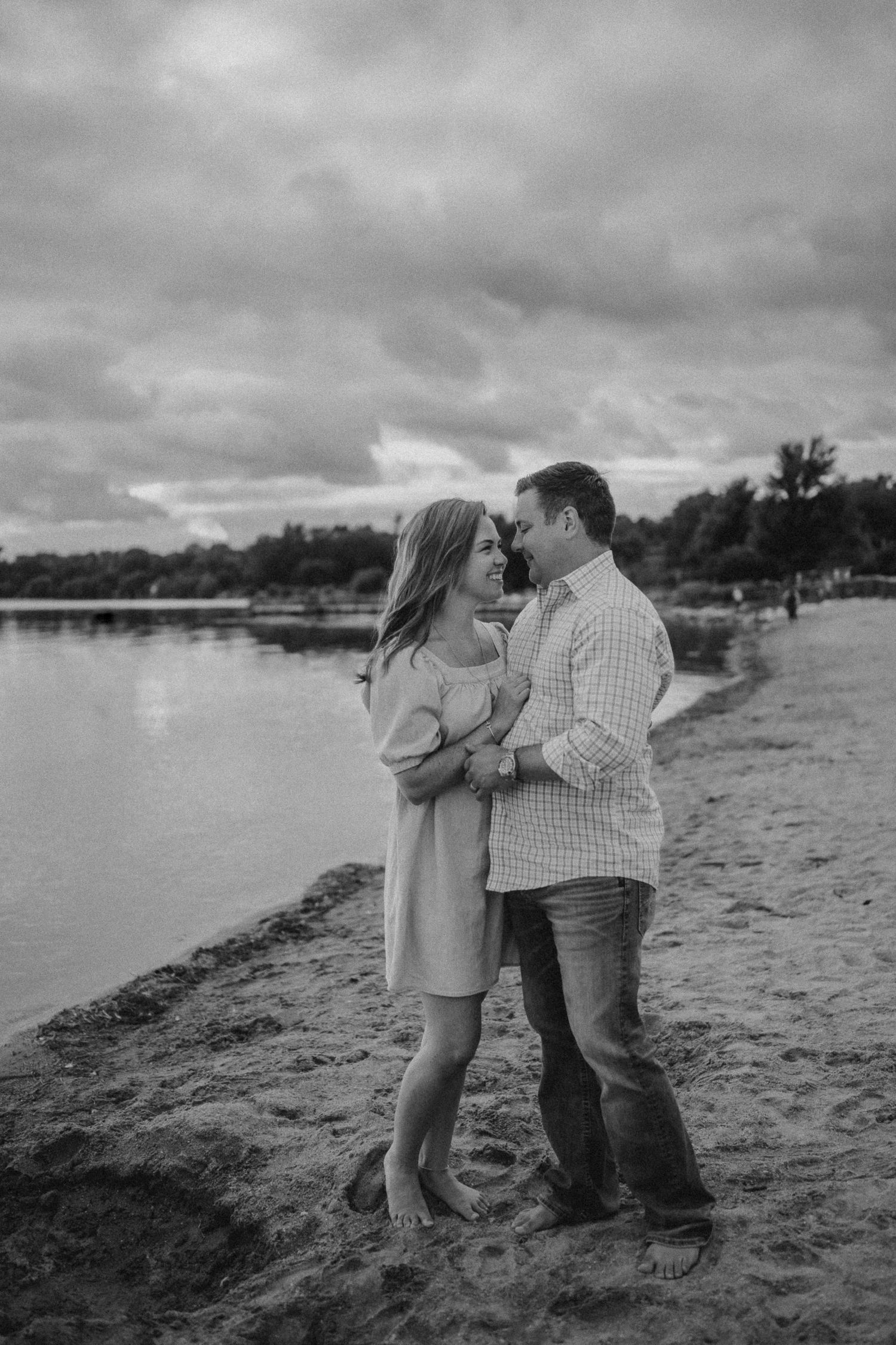 A romantic couple embraces on a sandy beach with stormy skies overhead.