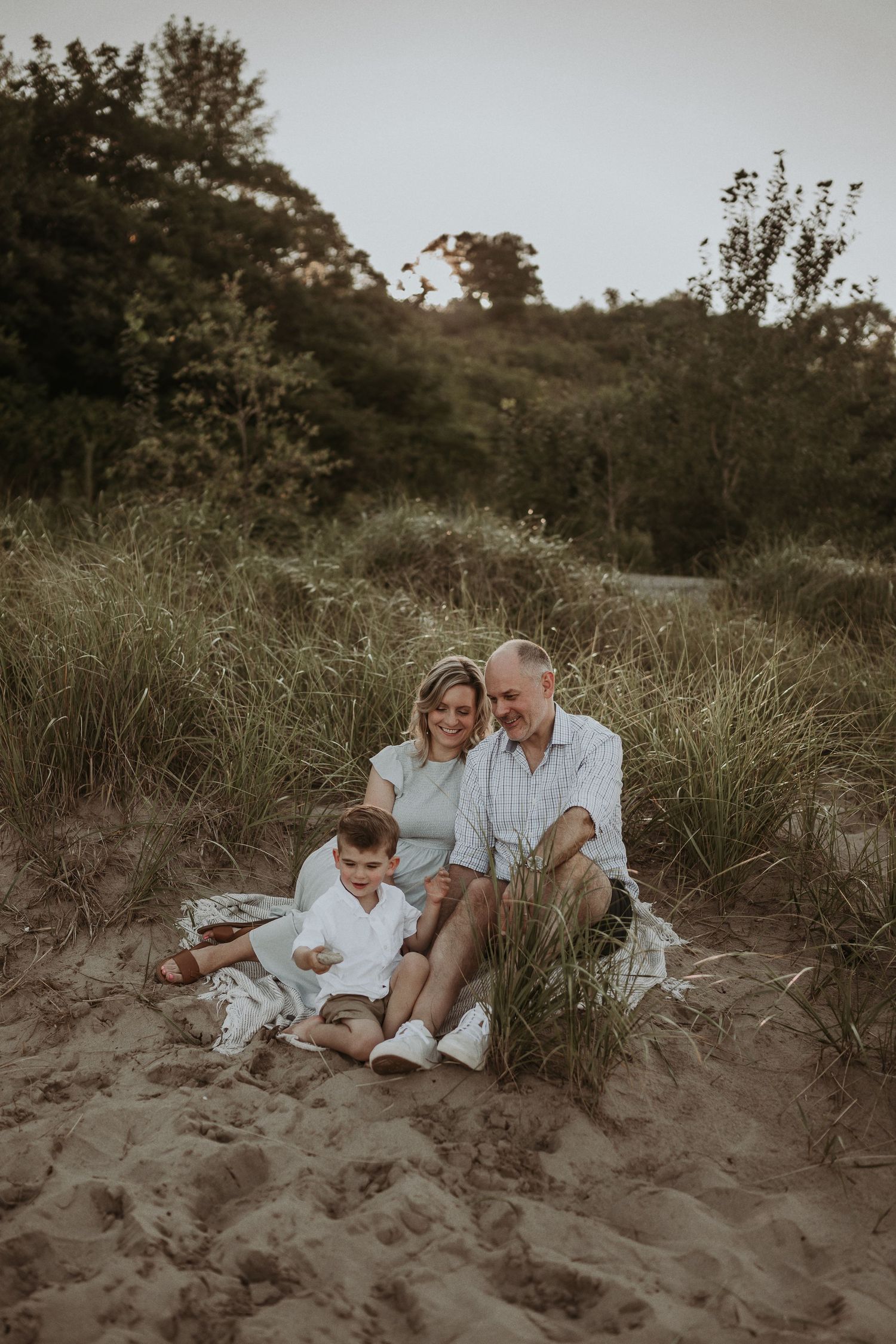 Family relaxes together on sandy dunes during sunset.