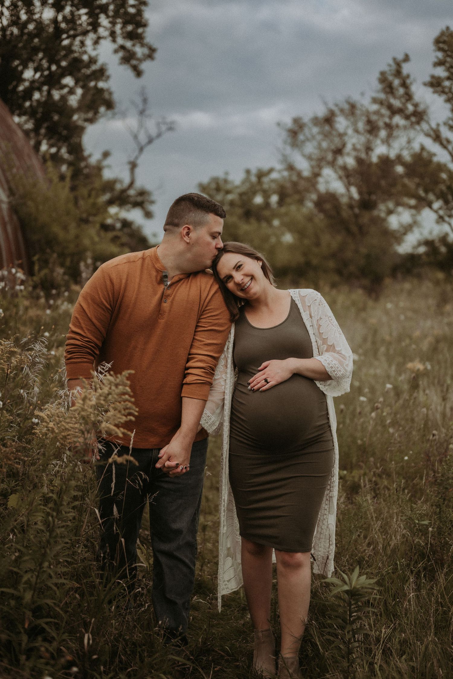 A tender moment captured during an outdoor maternity session in a meadow.