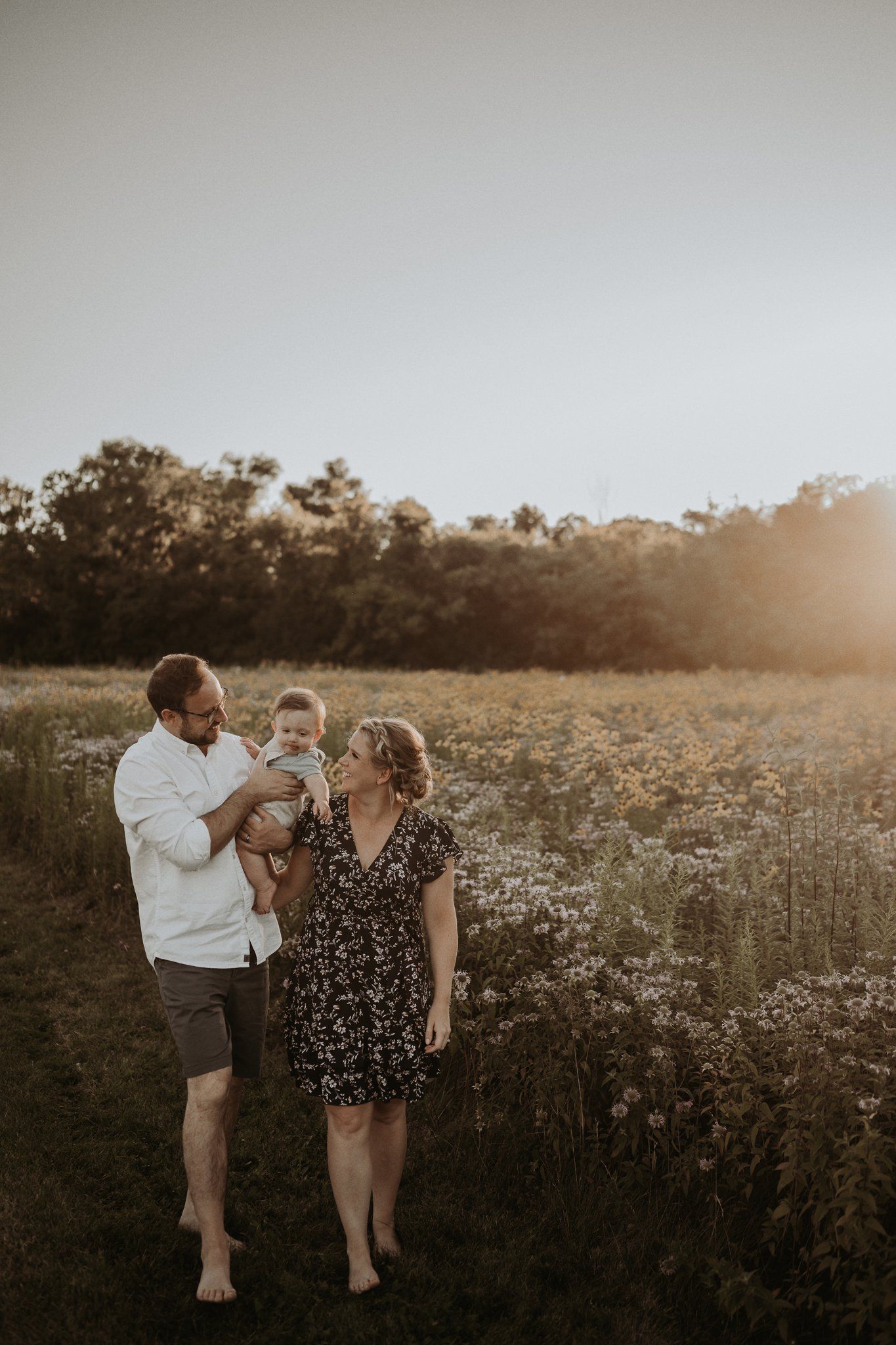 Family walks through blooming wildflower meadow during golden hour sunset.