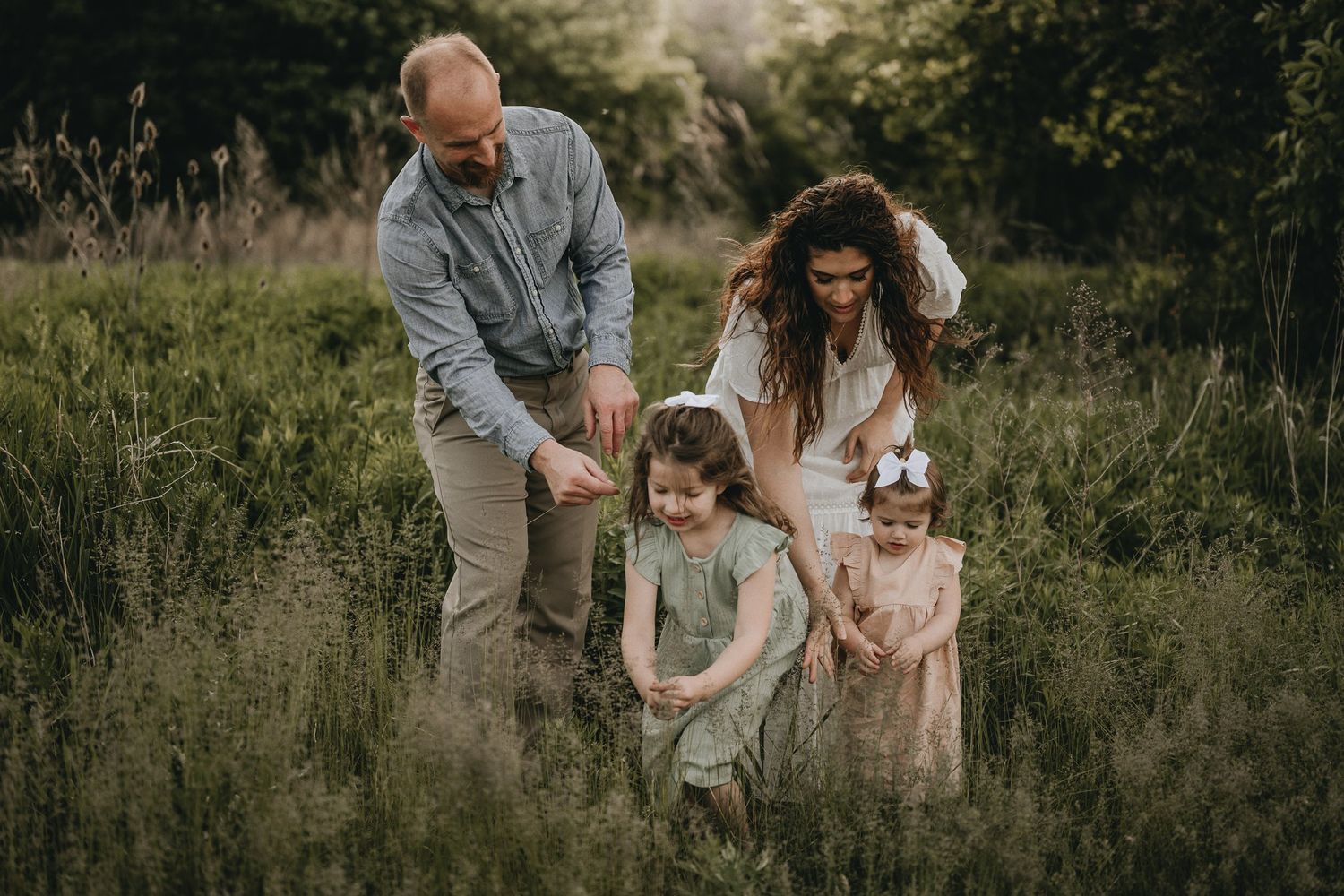 Candid family moment walking together through tall grass during sunset in matching neutral tones.