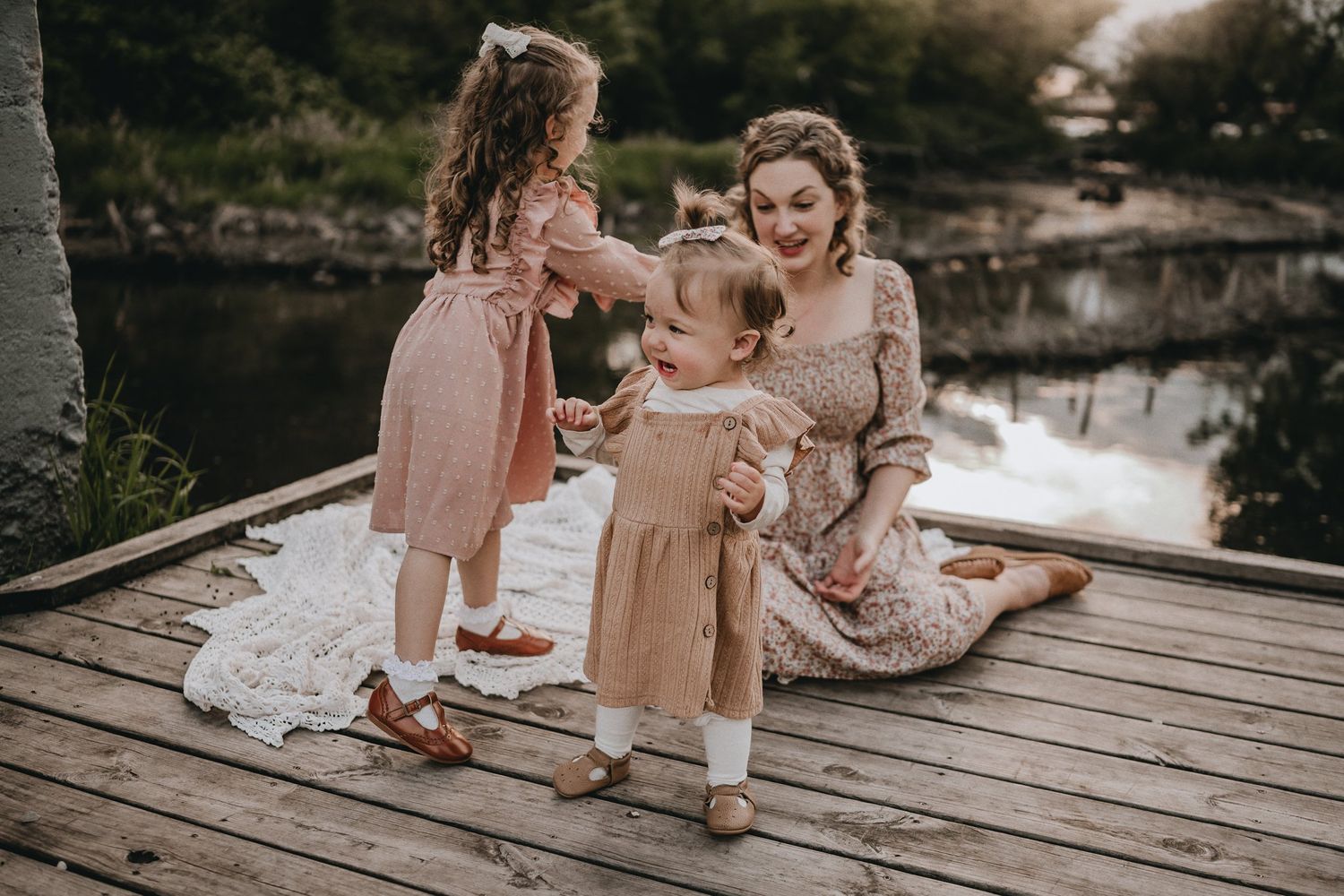 A heartwarming scene of people in pink dresses sharing a moment together on a wooden dock by a tranquil lake.