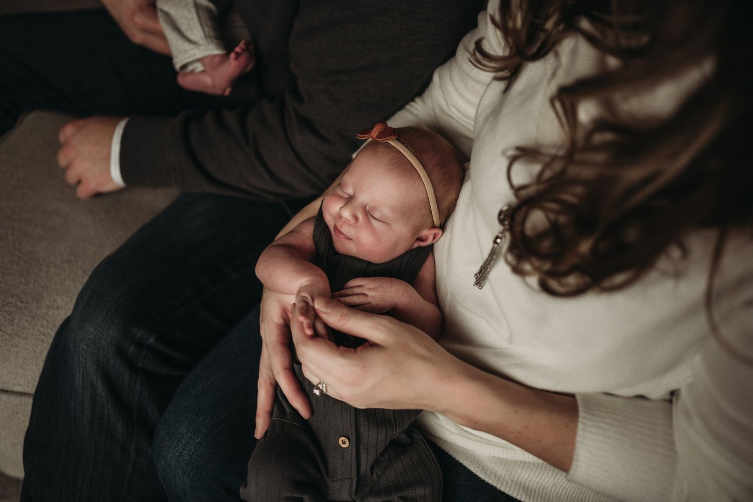 An intimate black and white photo of parents with newborn baby on couch.