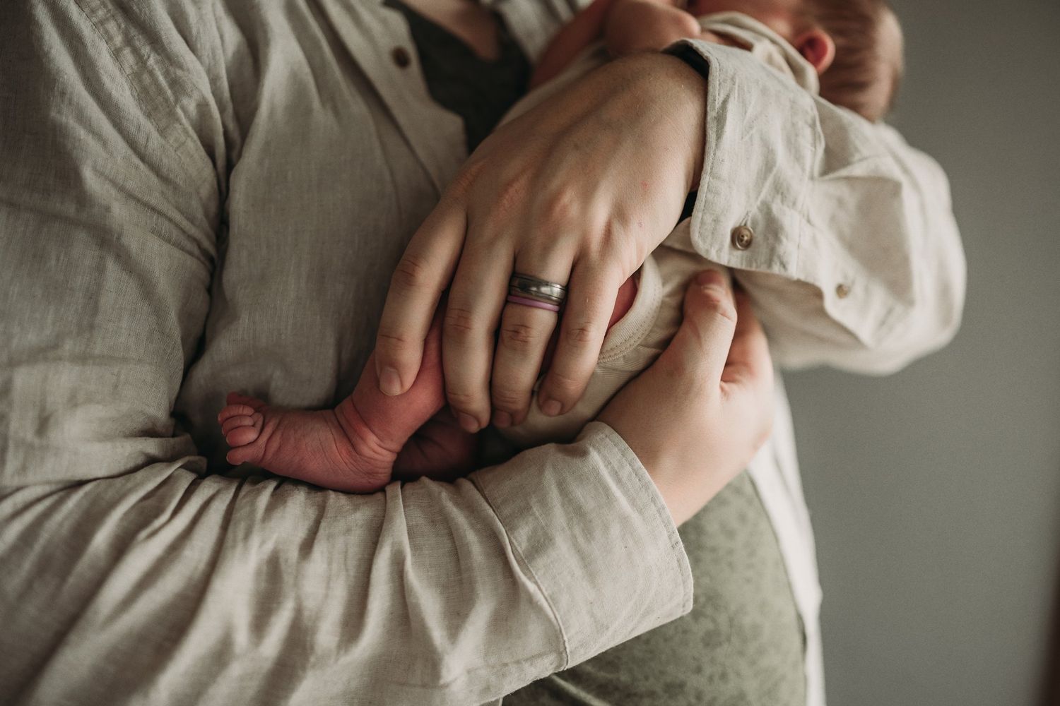 Close-up shot showing hands cradling a newborn's tiny feet against a light colored shirt.
