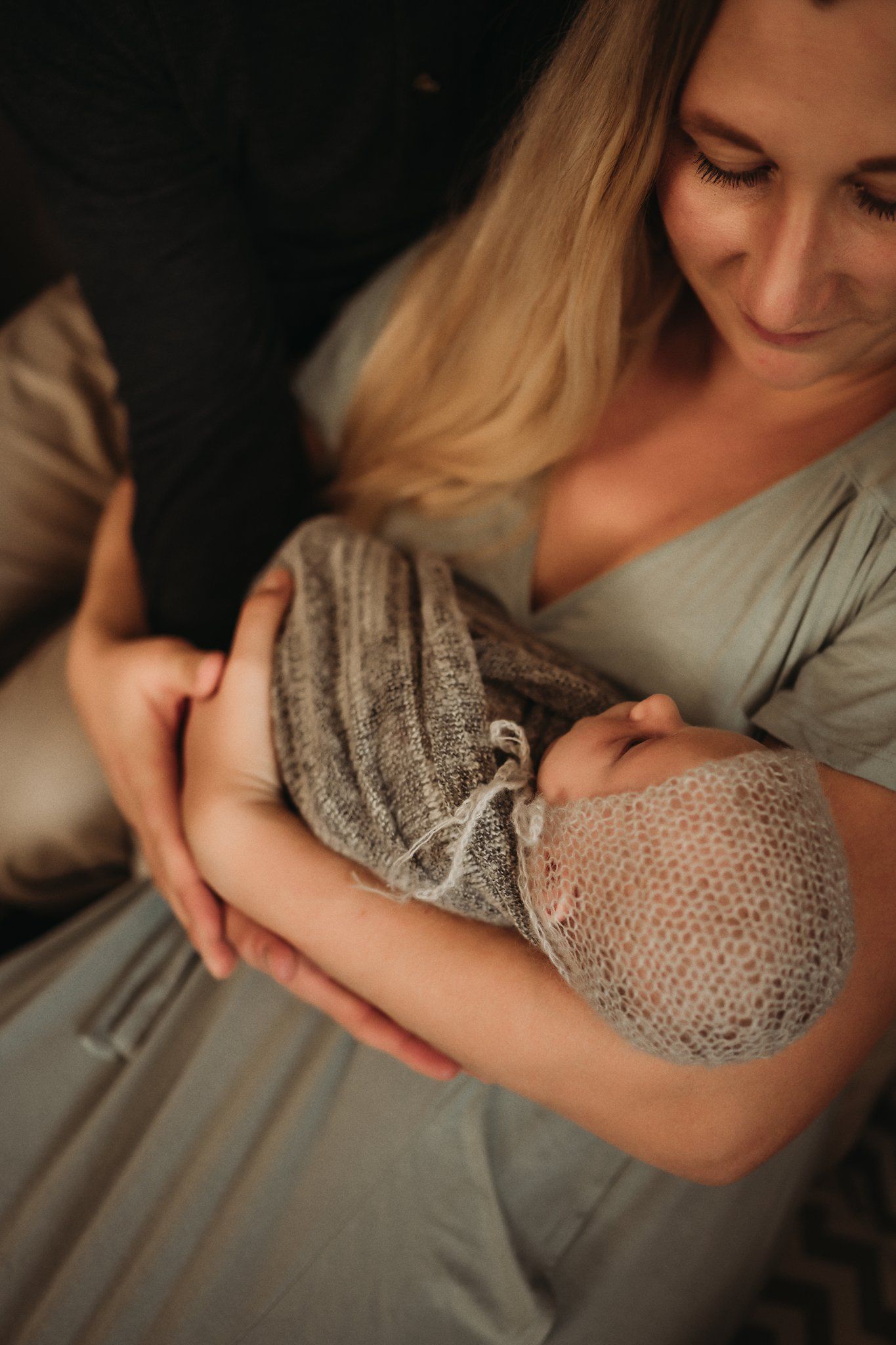 Gentle nurturing moment with baby wrapped in gray knit blanket.