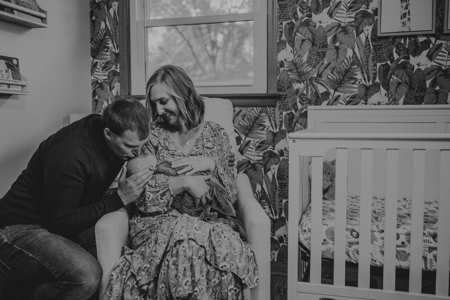 Intimate black and white photo of couple sharing tender moment in nursery with floral wallpaper.