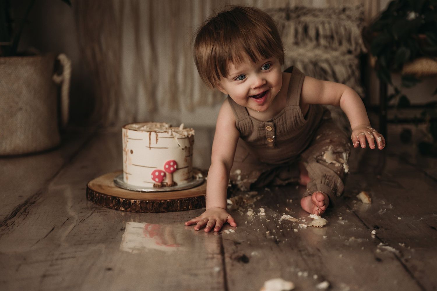 Joyful toddler laughing while playing with cake during rustic-themed cake smash photo session.