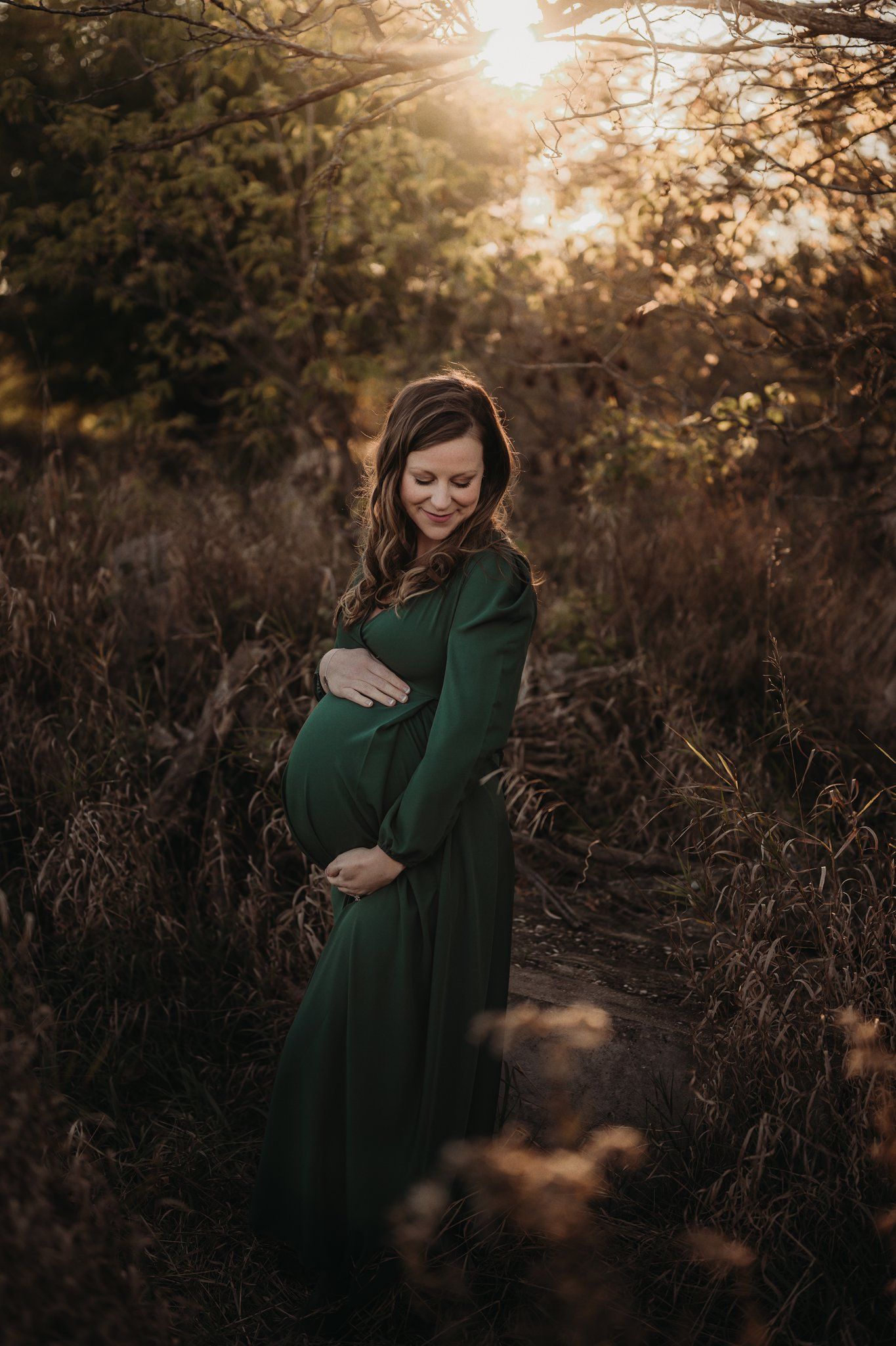 An outdoor maternity photo showing an expecting mother in a green dress at sunset.