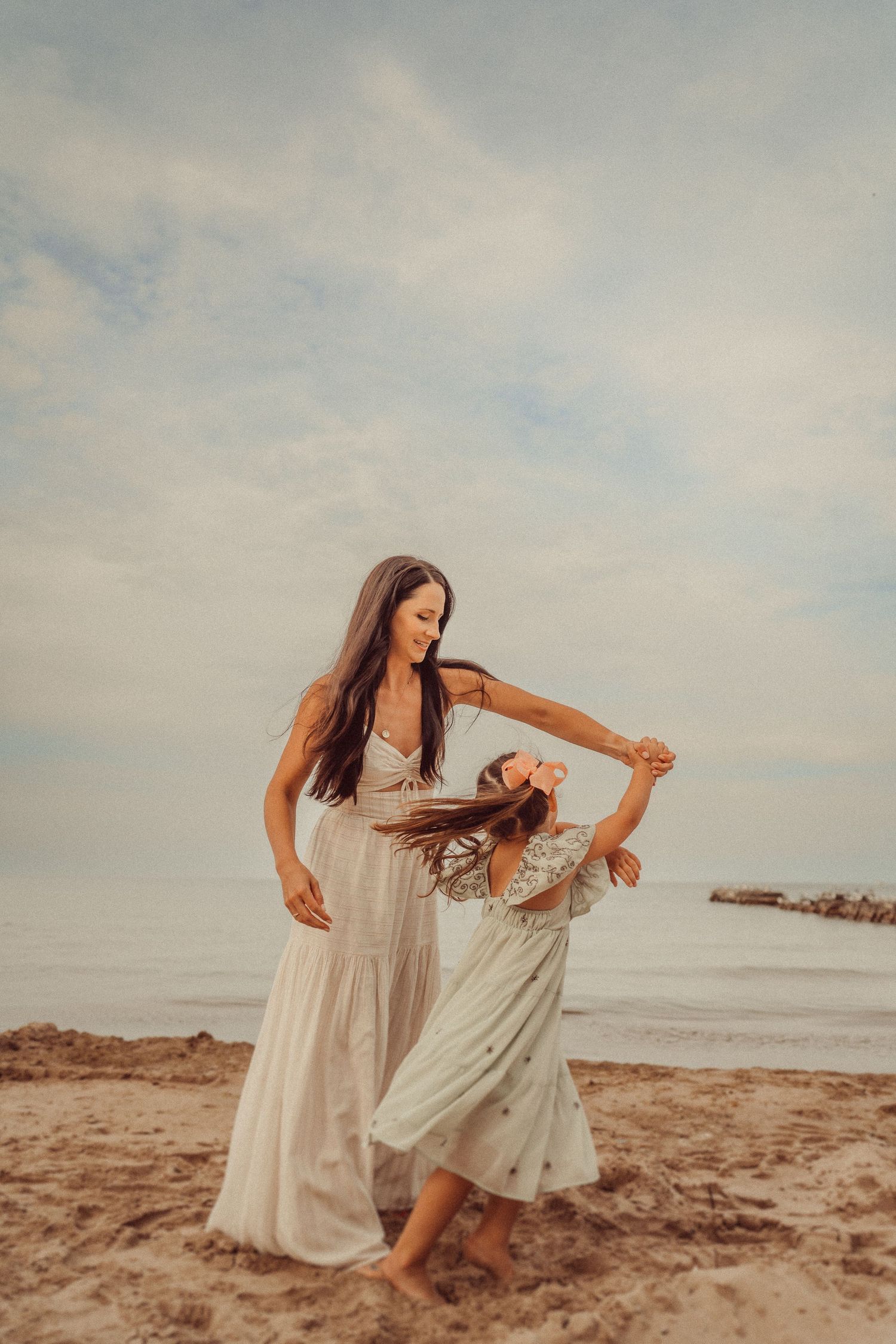 Two people in white dresses dance together on a sandy beach at golden hour.