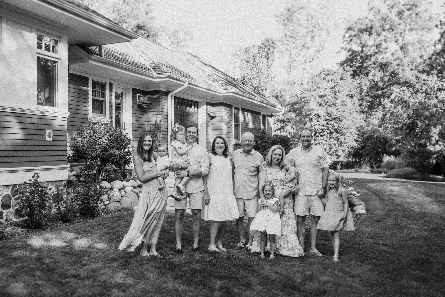 A black and white photograph of a group gathering on a lawn in front of a craftsman-style house.