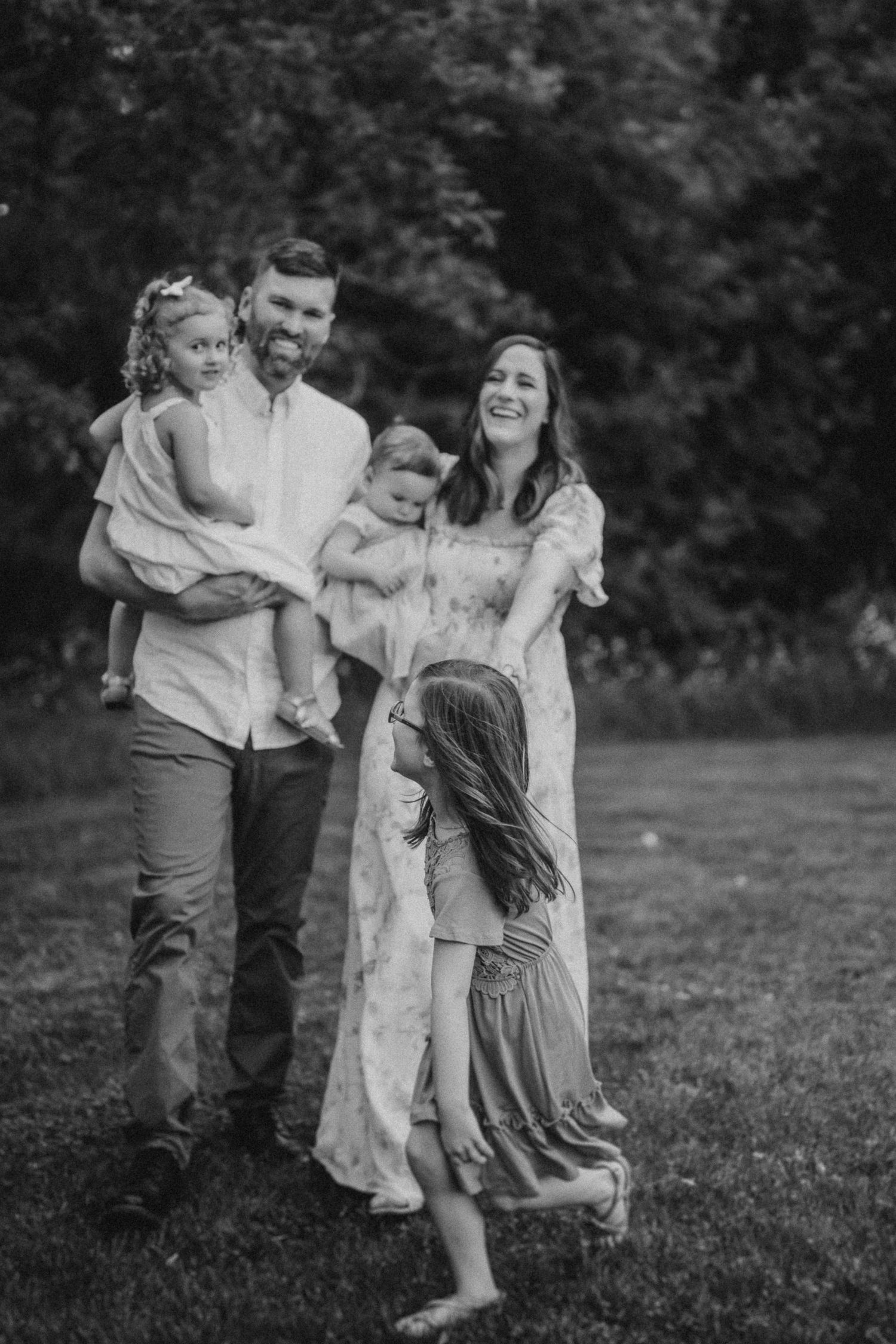A candid family moment captured in black and white on a grassy field with trees in background.