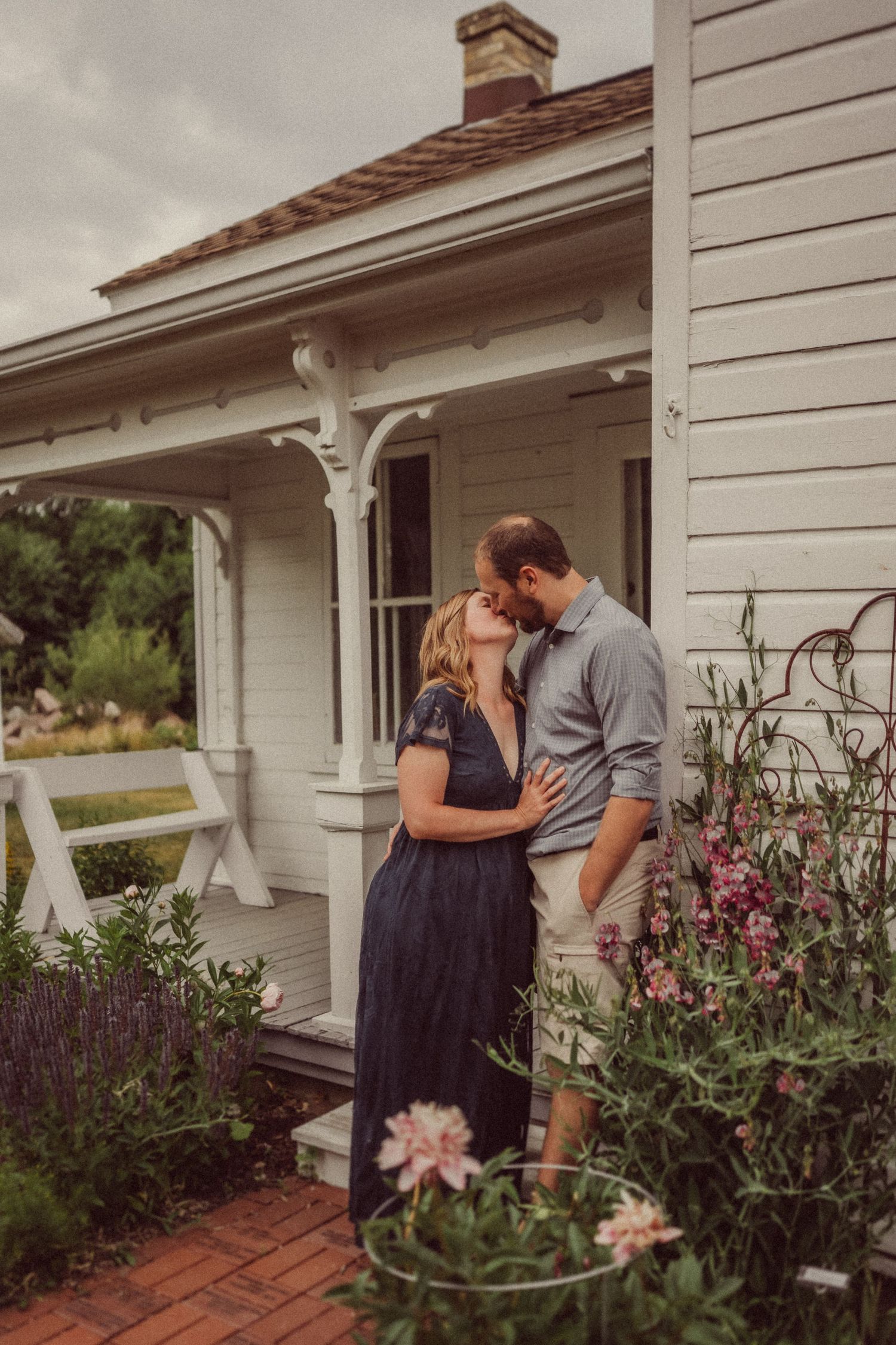 Couple sharing romantic moment on porch of white farmhouse with garden.