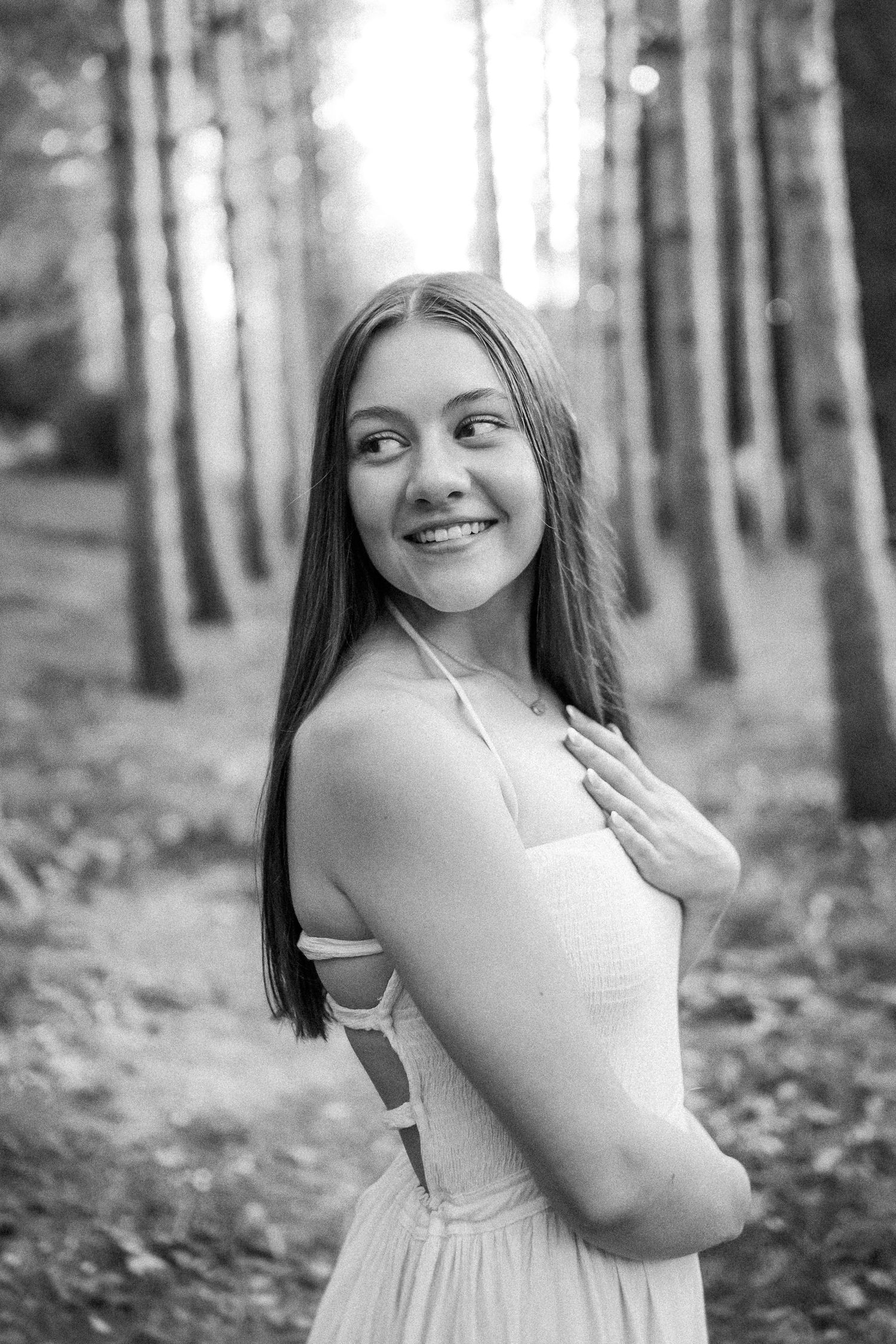 Black and white portrait series showing joyful expressions and poses among towering pine trees in a forest setting.