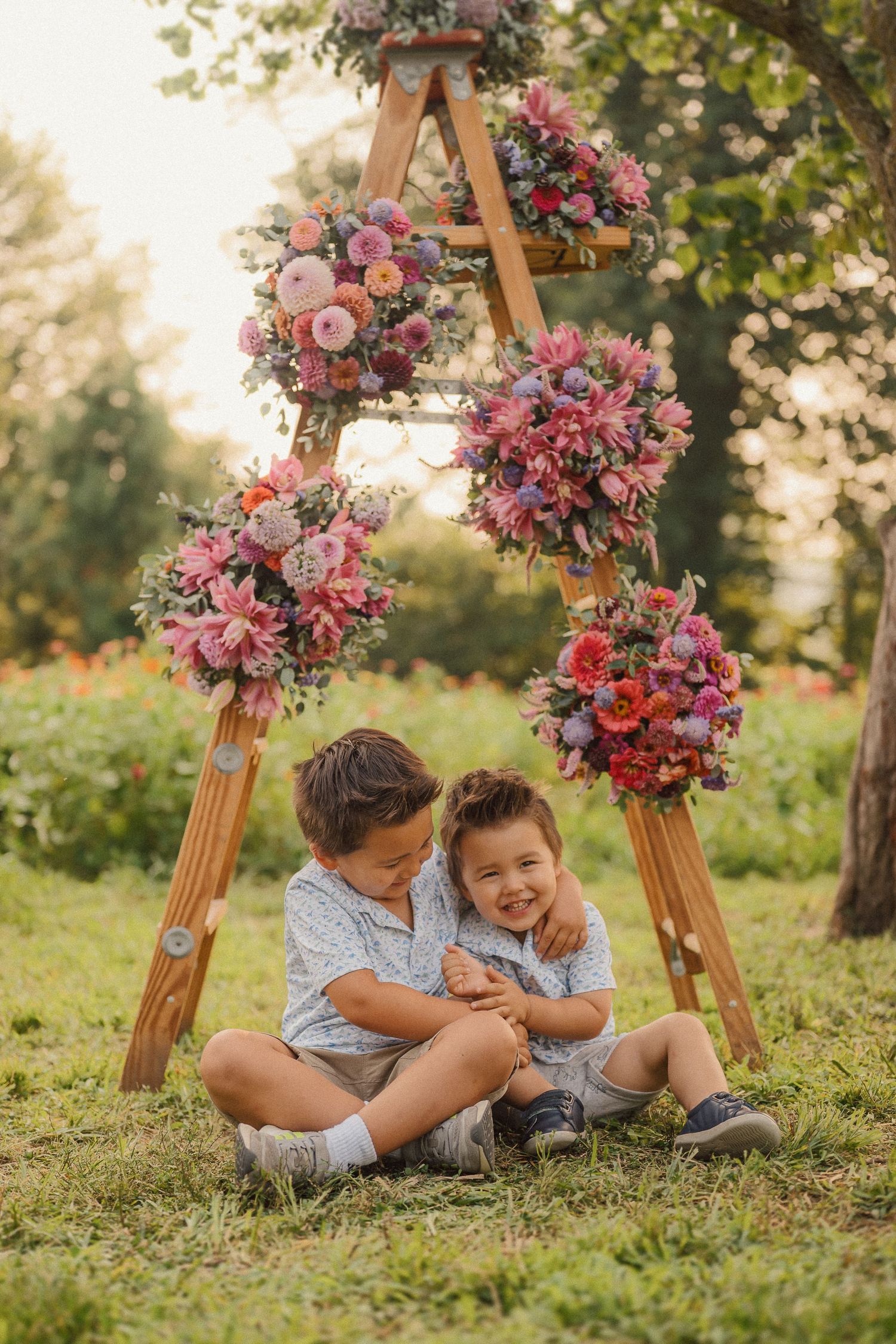 Sweet outdoor family moment captured on grassy hill with beautiful floral decorations and wooden swing frame.