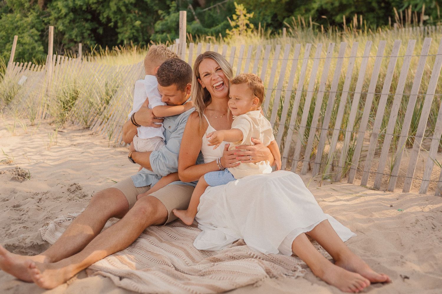 Relaxed beach portrait session with soft golden light and sand fencing in background.
