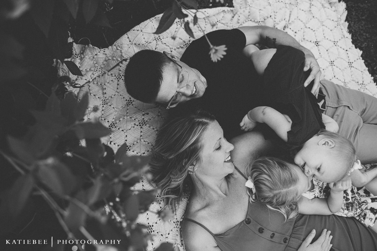 Black and white image of family cuddle moment on white blanket outdoors.