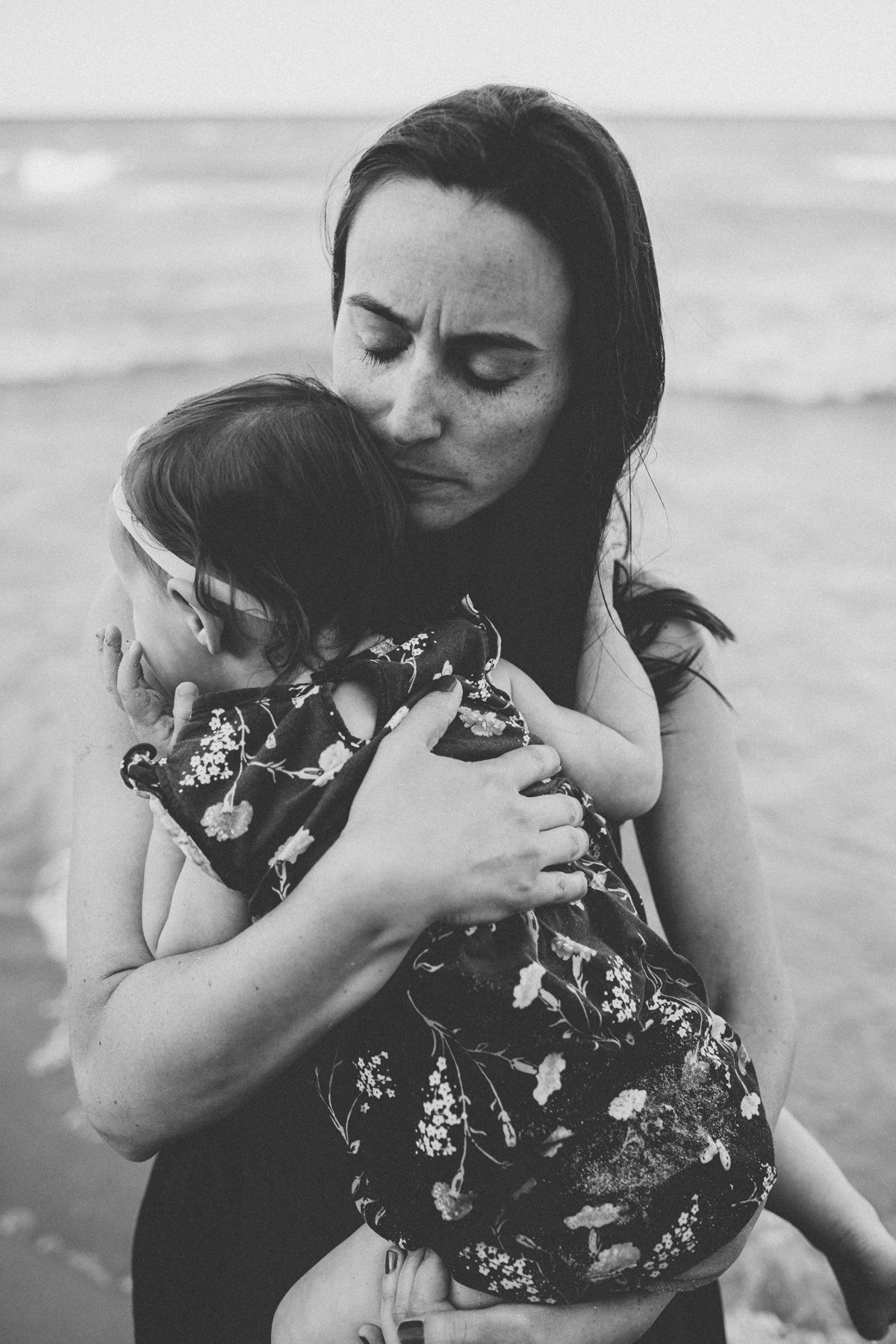 A tender monochromatic moment captured on a beach as mother and child share a loving embrace.