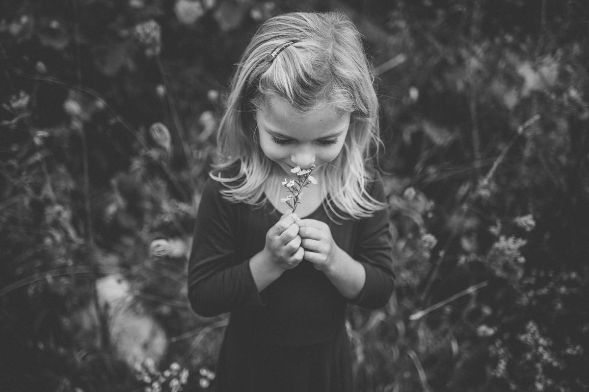A black and white photo of a child examining a small flower in their hands.