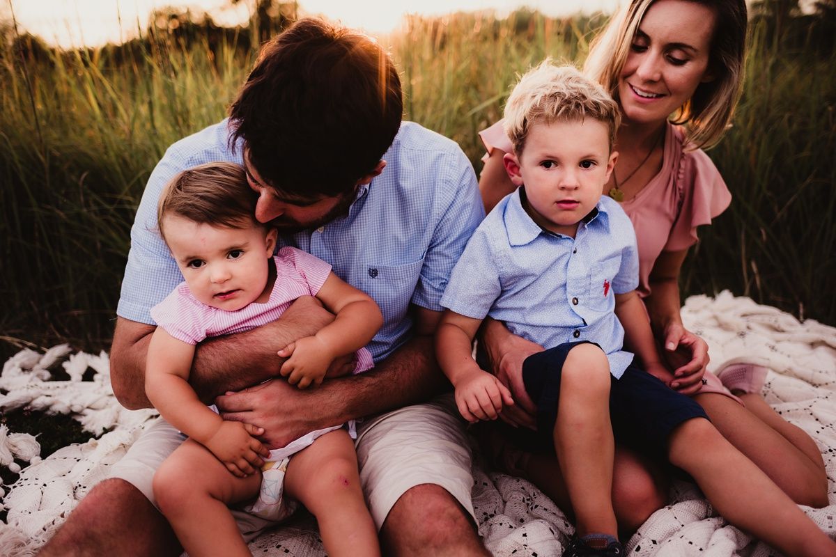 Intimate family portrait on a white blanket in tall grass during sunset.