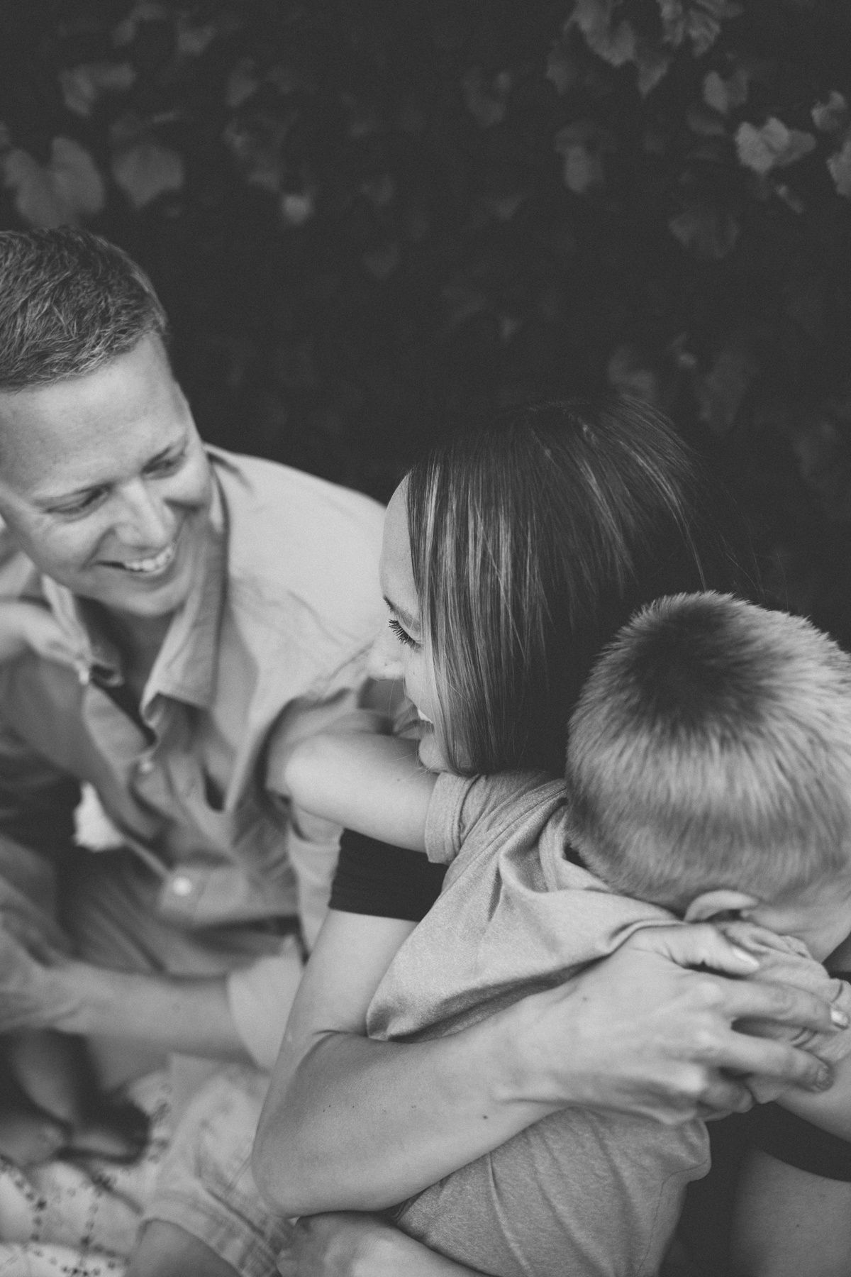 Family sharing a joyful laugh together in a candid black and white outdoor portrait.
