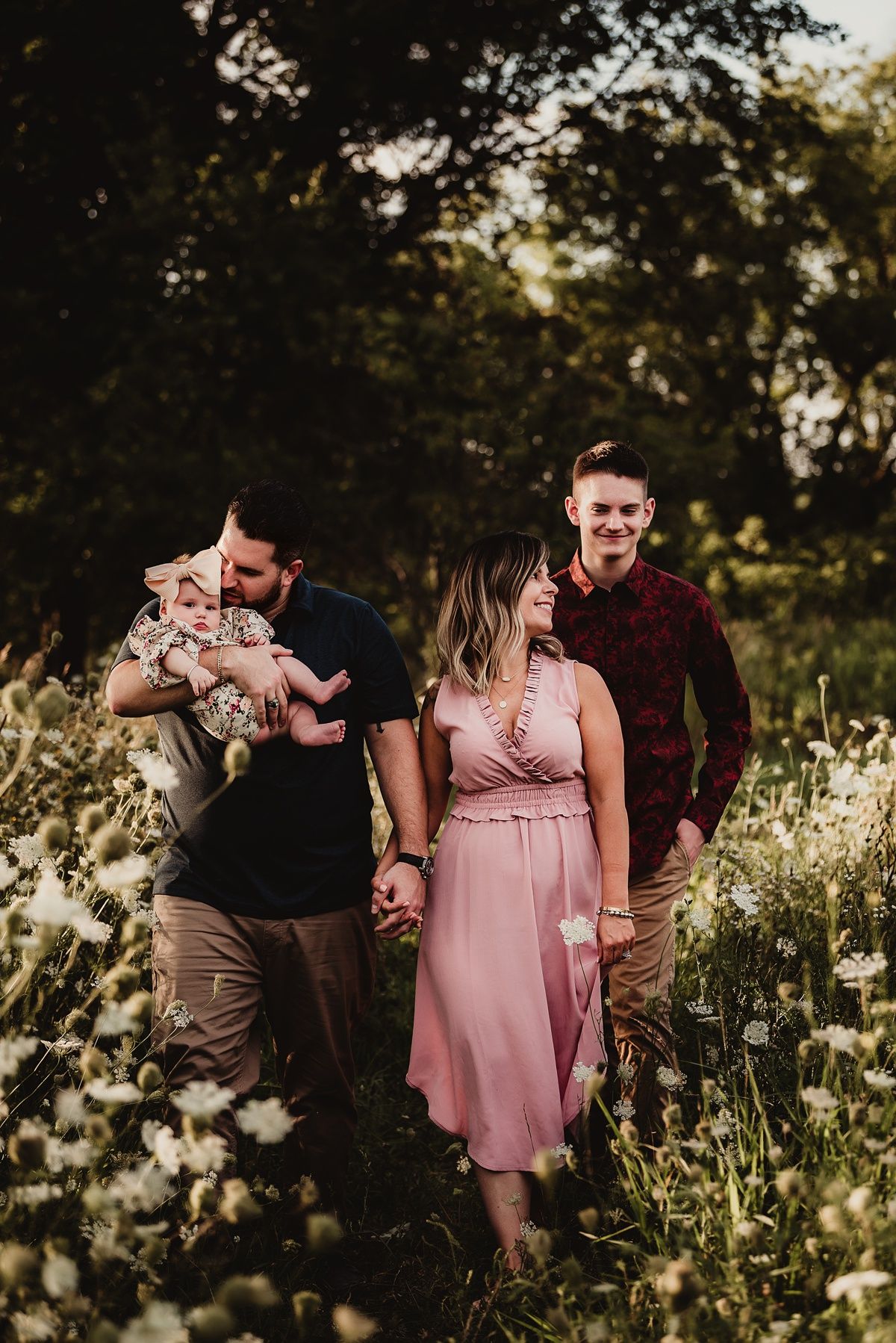 Group walking through meadow at golden hour with baby in floral outfit.