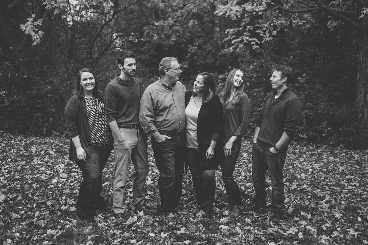 Group standing together on fallen autumn leaves in black and white photograph.