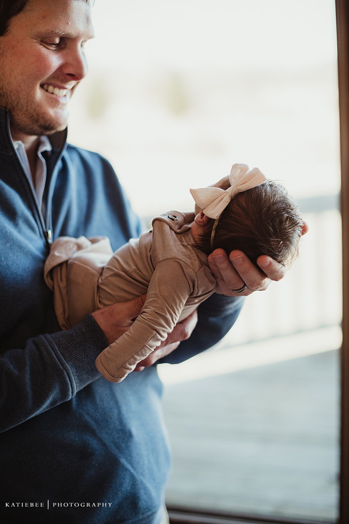 A tender moment as a navy blue clad caregiver cradles a tiny infant in a beige outfit near a window.