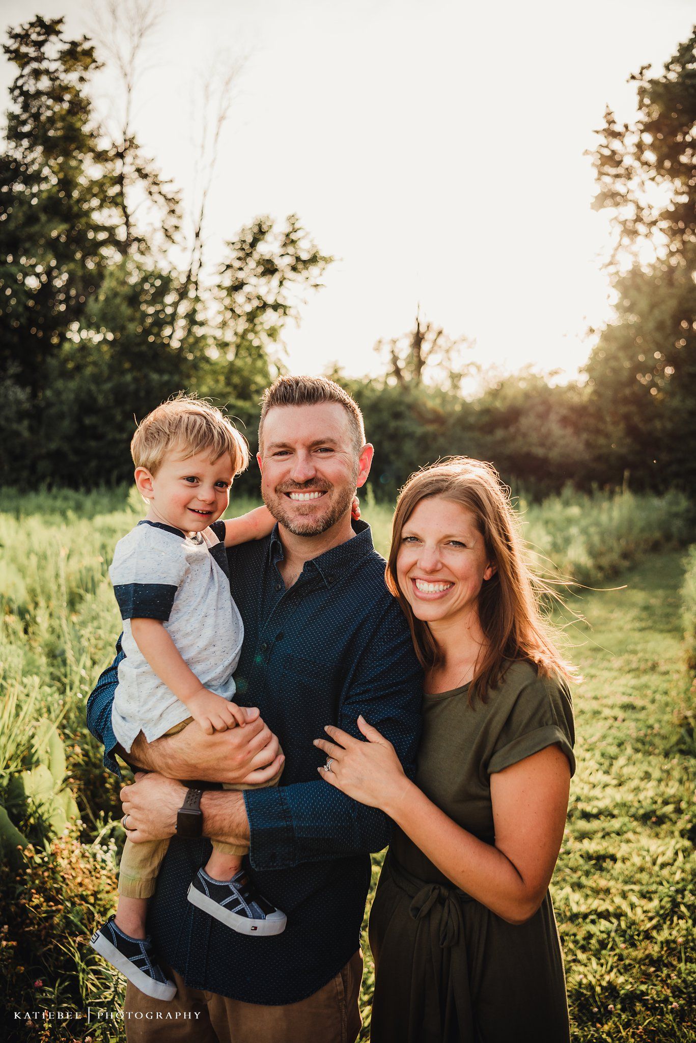 Family of three sharing an affectionate moment together in a sunlit meadow.