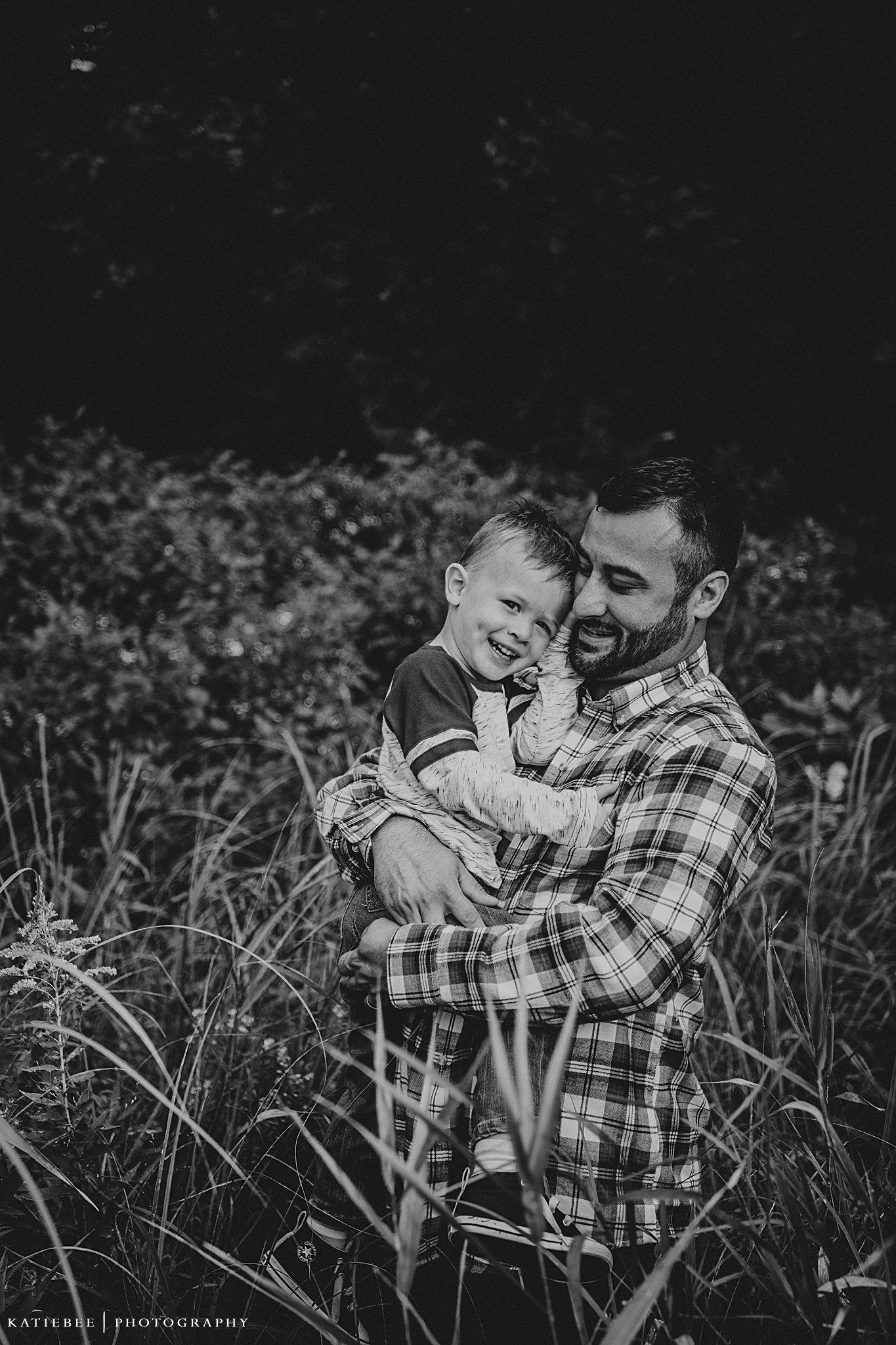 Black and white portrait of two people sharing a tender moment in tall grass.