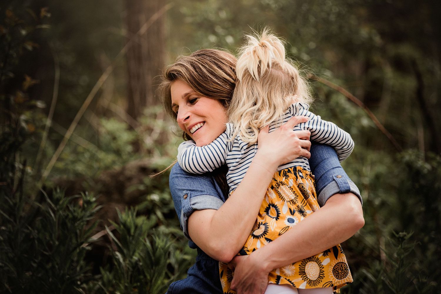 A tender embrace in nature with denim and stripes against a soft forest backdrop.