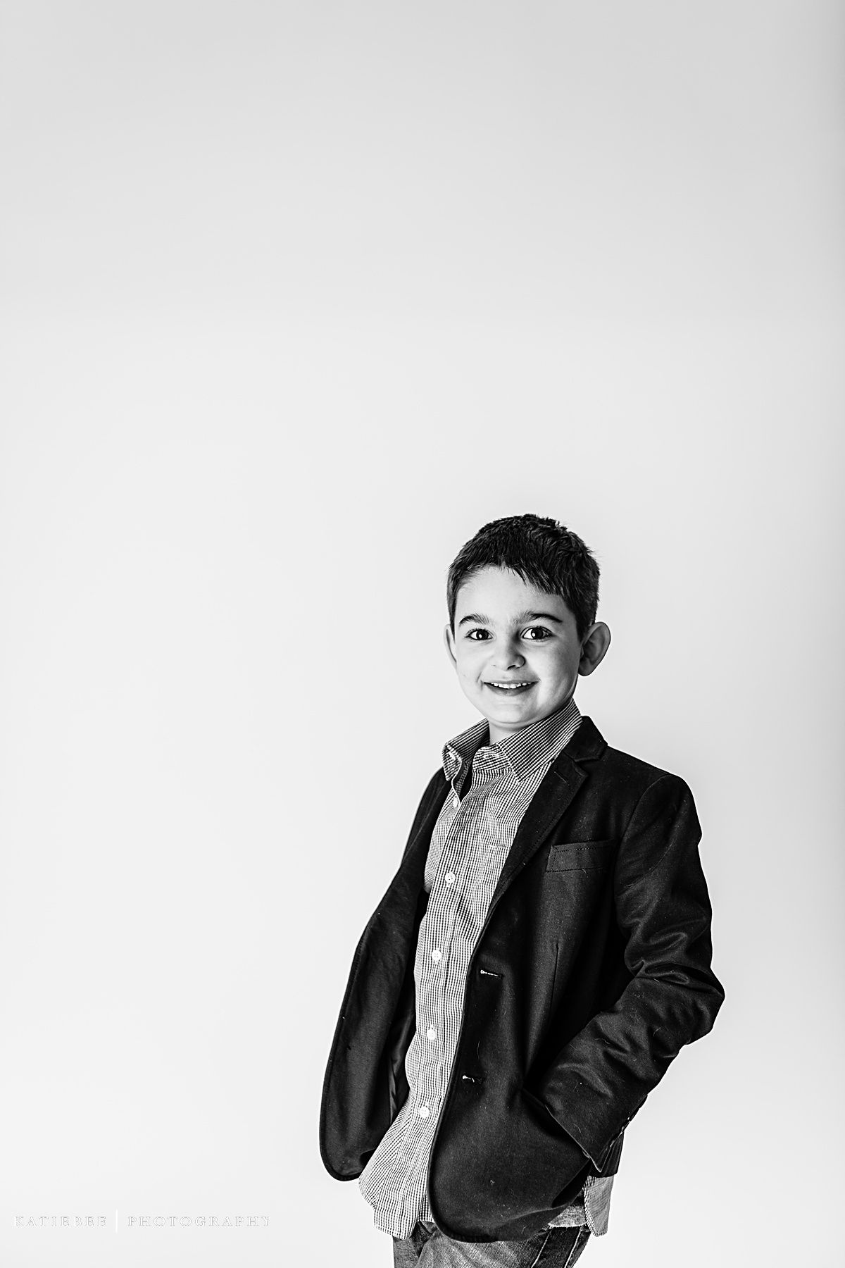 Black and white studio portrait of child in blazer looking off to side with slight smile.