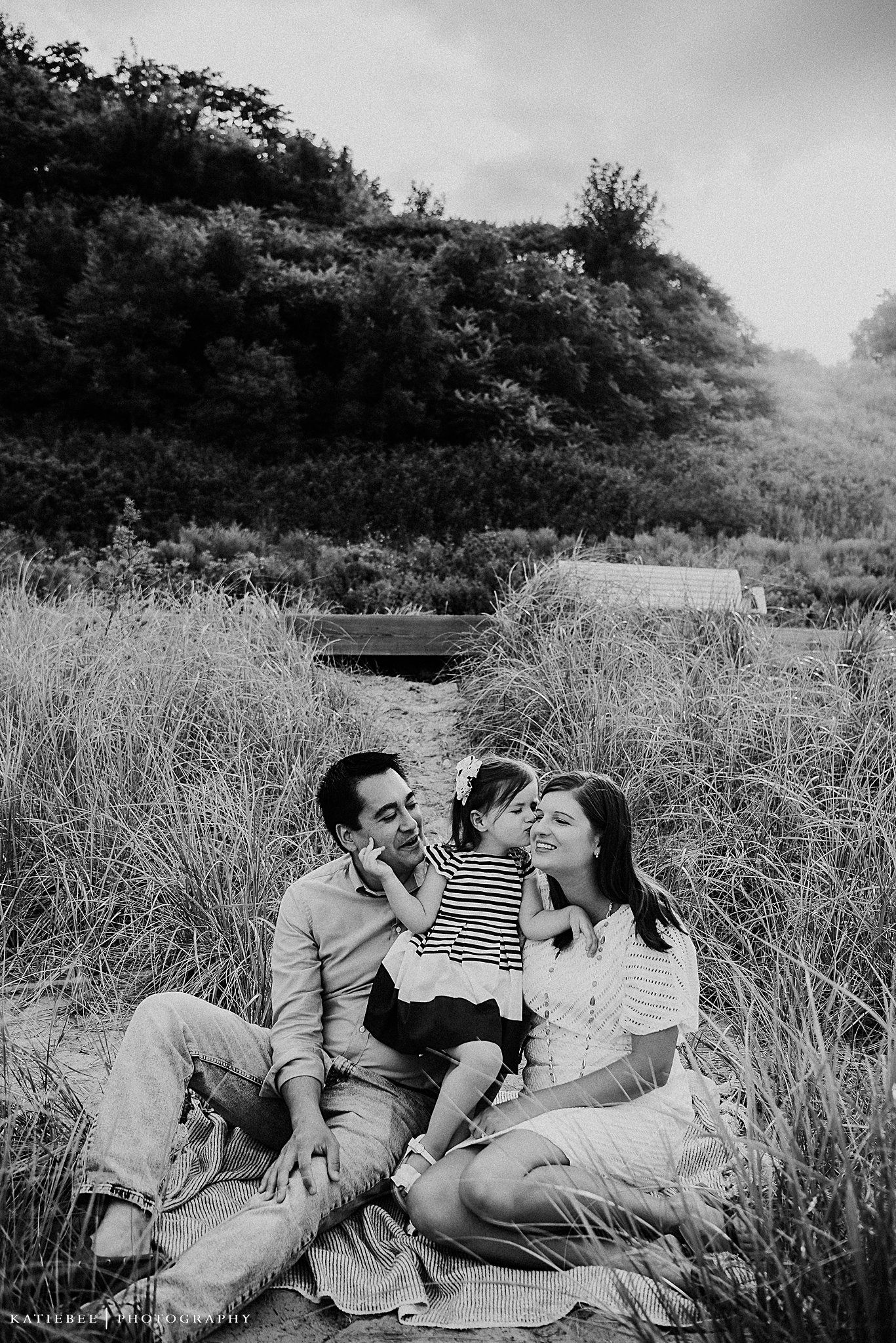 A family shares an intimate moment while sitting on a picnic blanket surrounded by tall grass.