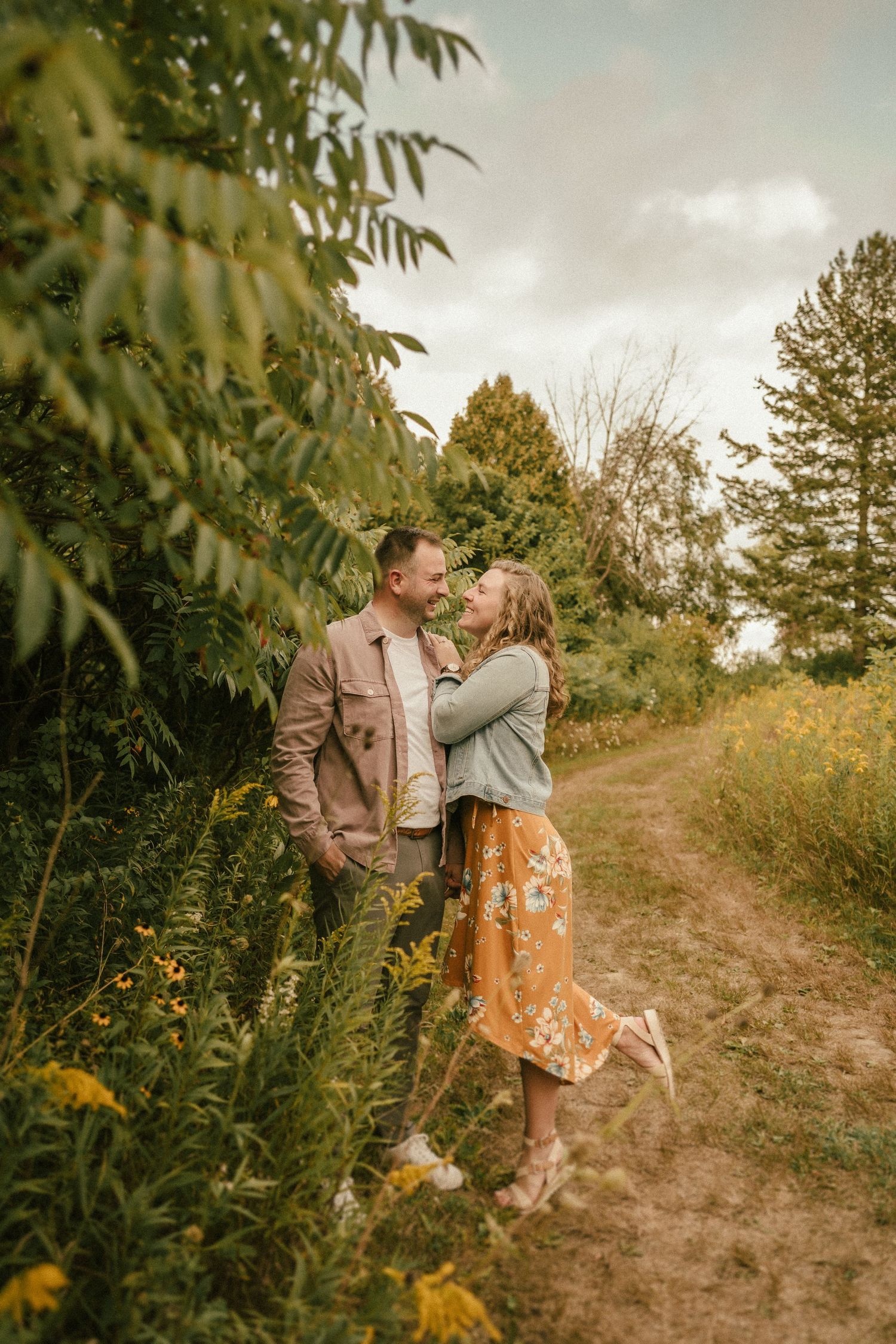 Romantic outdoor portrait on nature trail with wildflowers and trees in background.