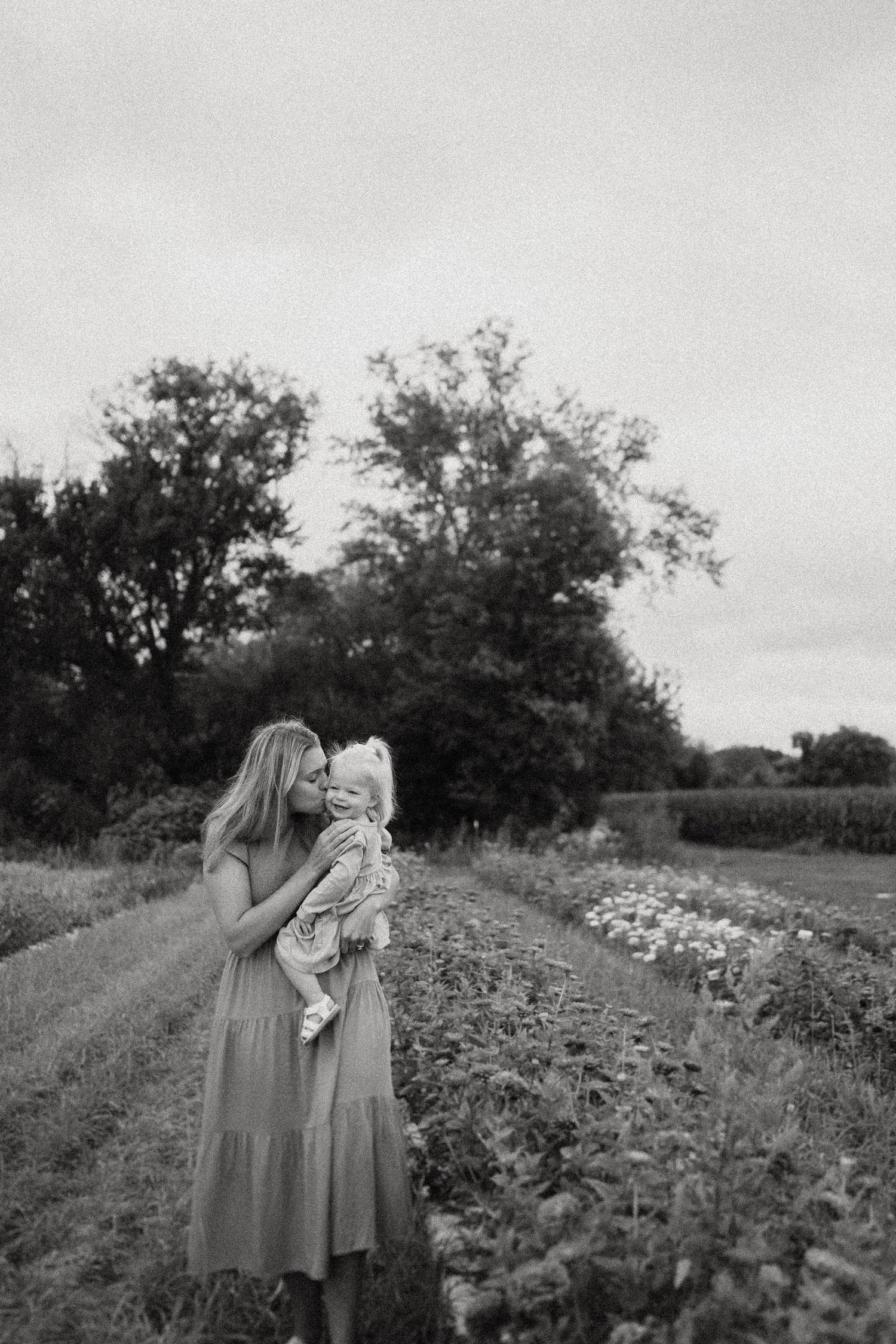 A tender black and white portrait in a flower field with trees in the background.