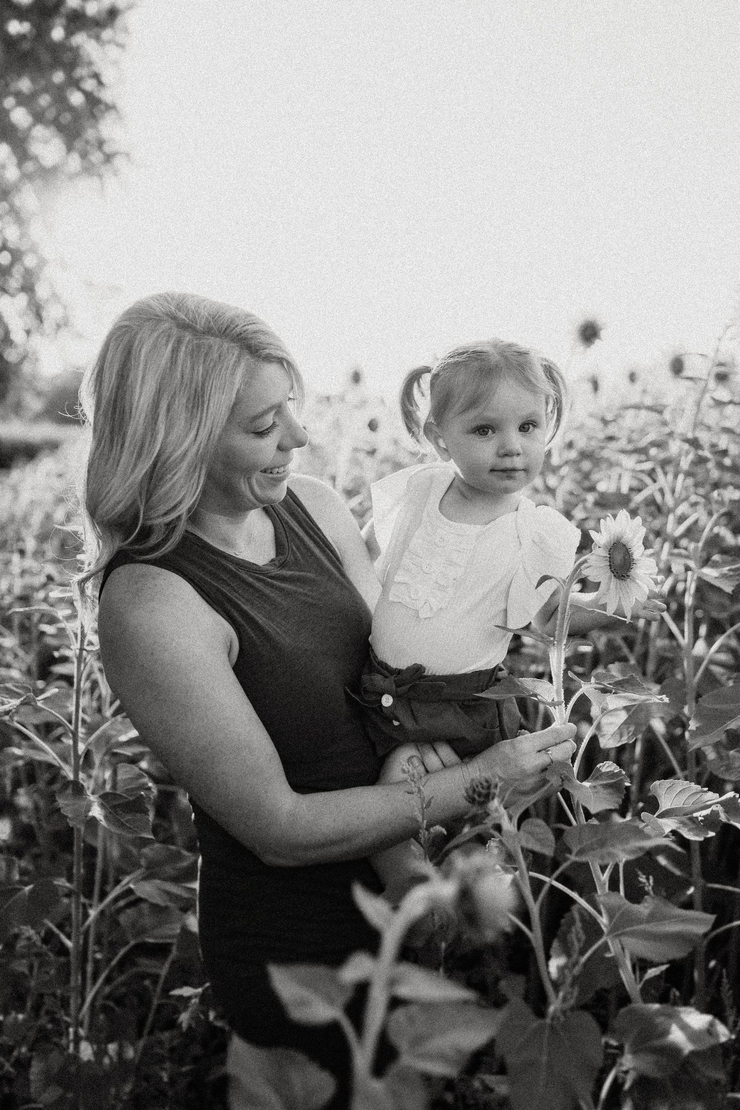 Black and white portrait of parent and child among blooming sunflowers.