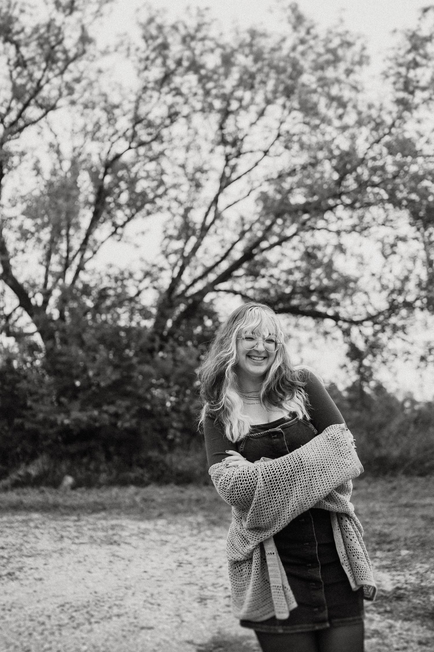 Black and white portrait showing joyful expression against tree silhouettes.