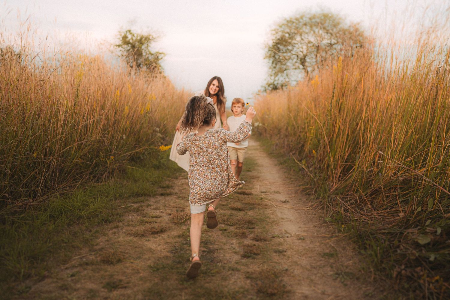 Family members walking down dirt path surrounded by tall golden grass at sunset.