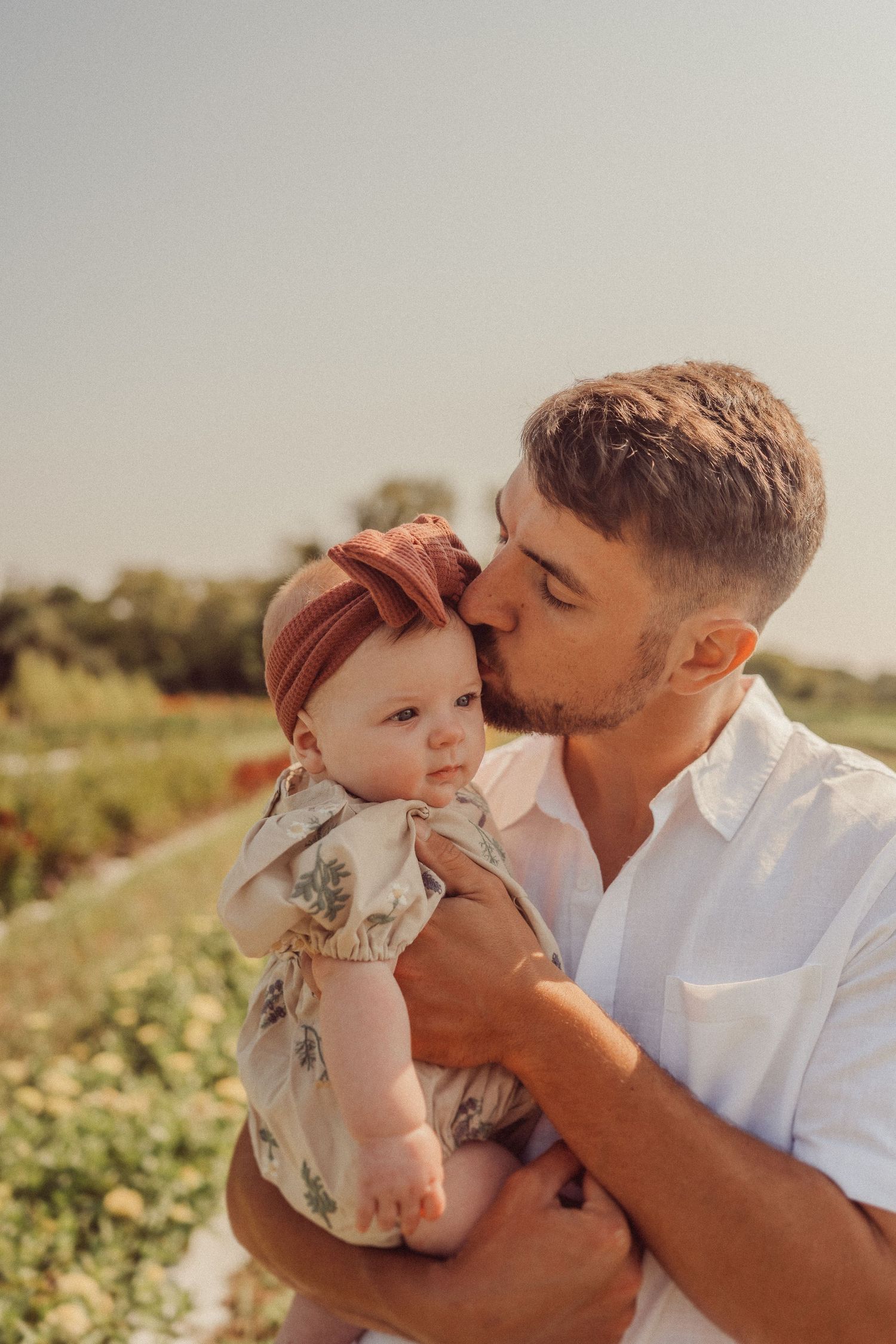 A sweet parental moment captured in warm sunlight among flowering plants.