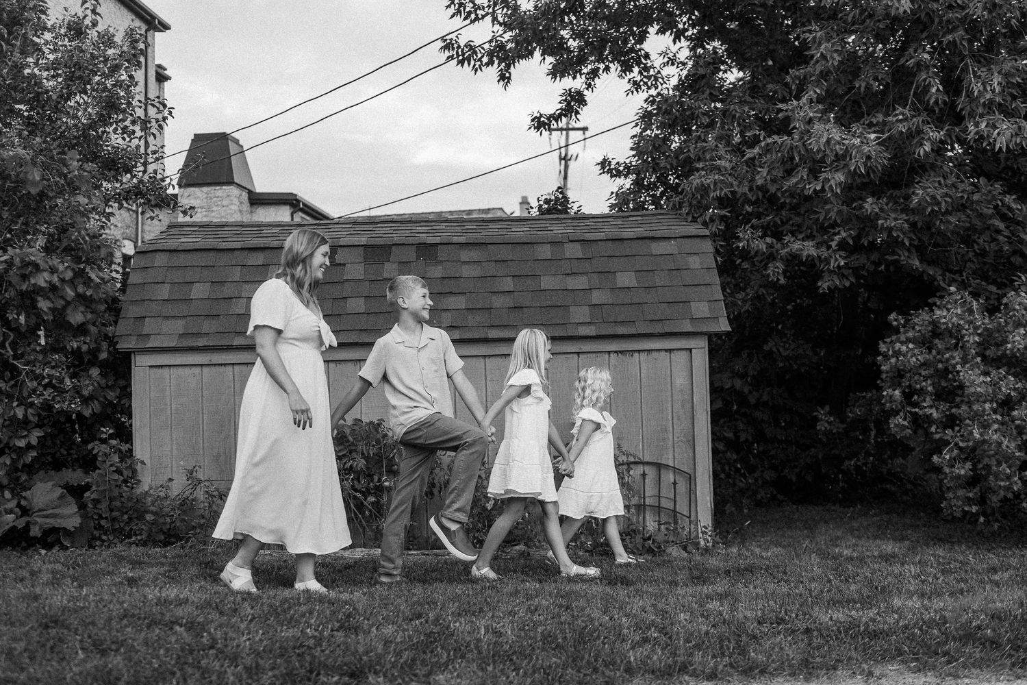 A family walks together in white dresses through a backyard garden in black and white.
