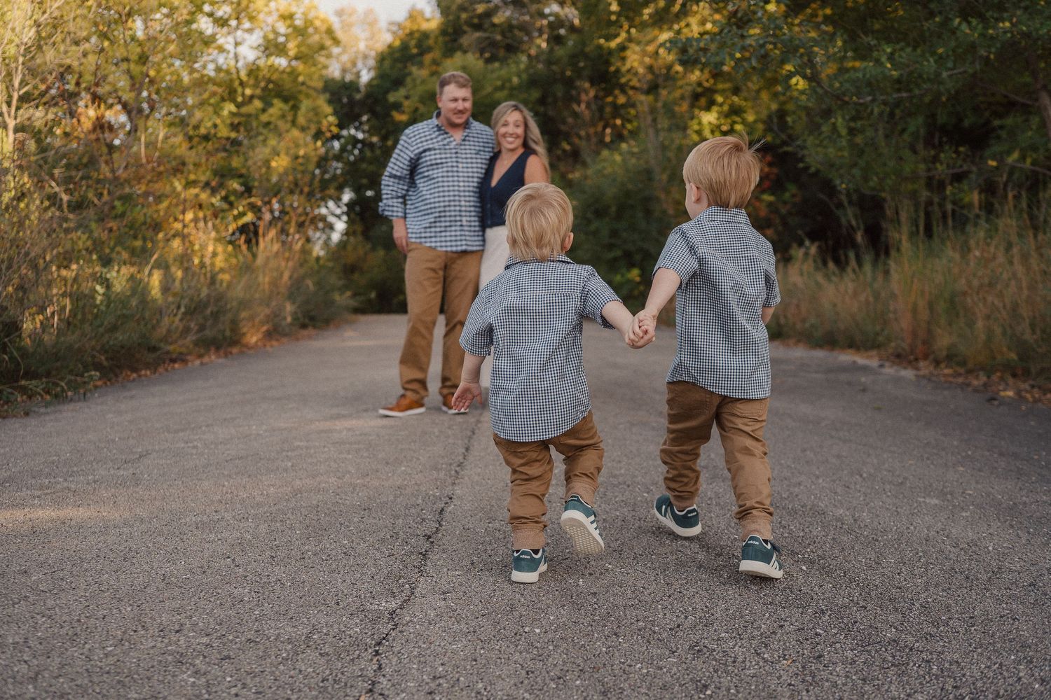 People walking and holding hands on a paved path surrounded by autumn foliage.
