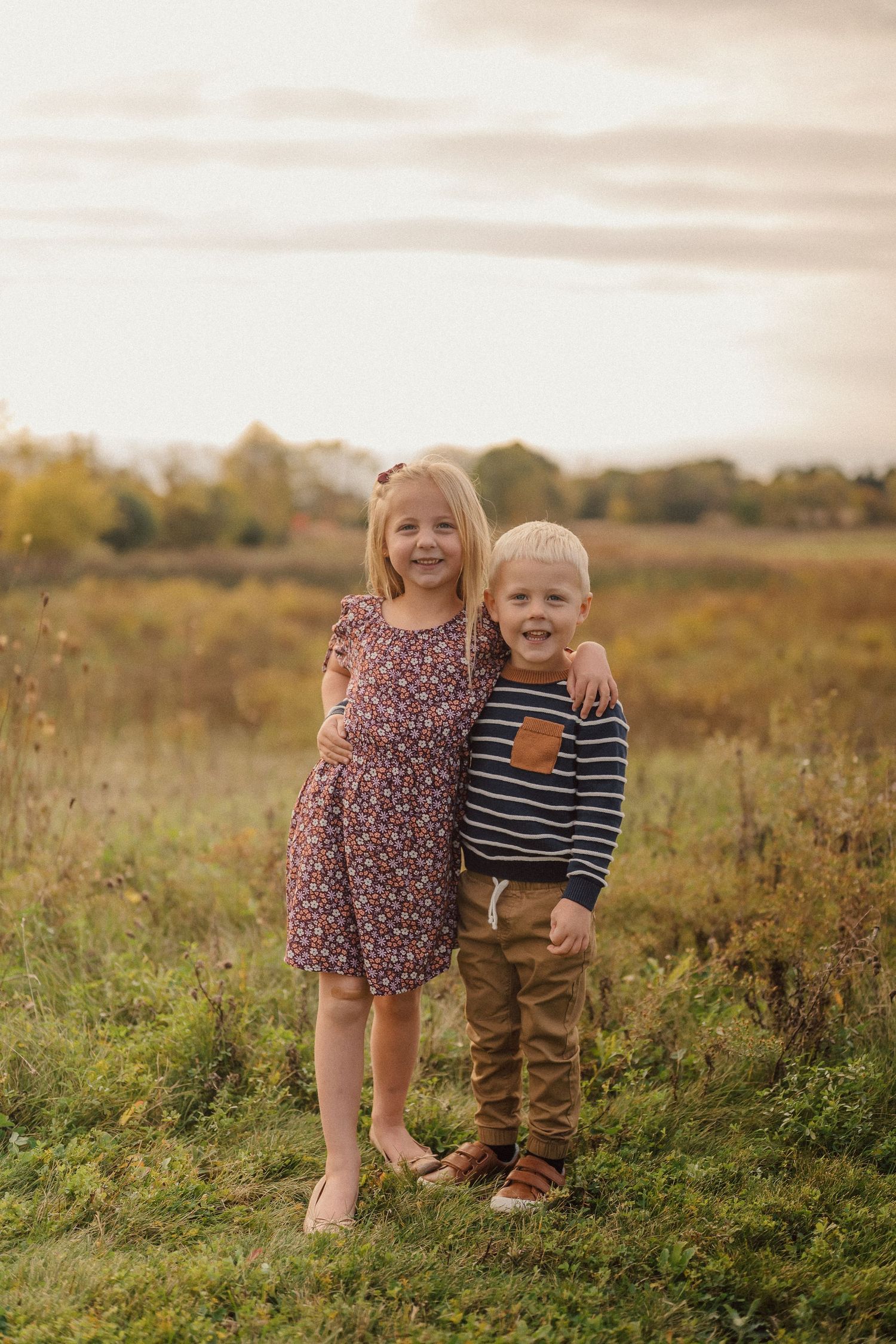 Two young children playing and laughing together in a golden field at sunset.